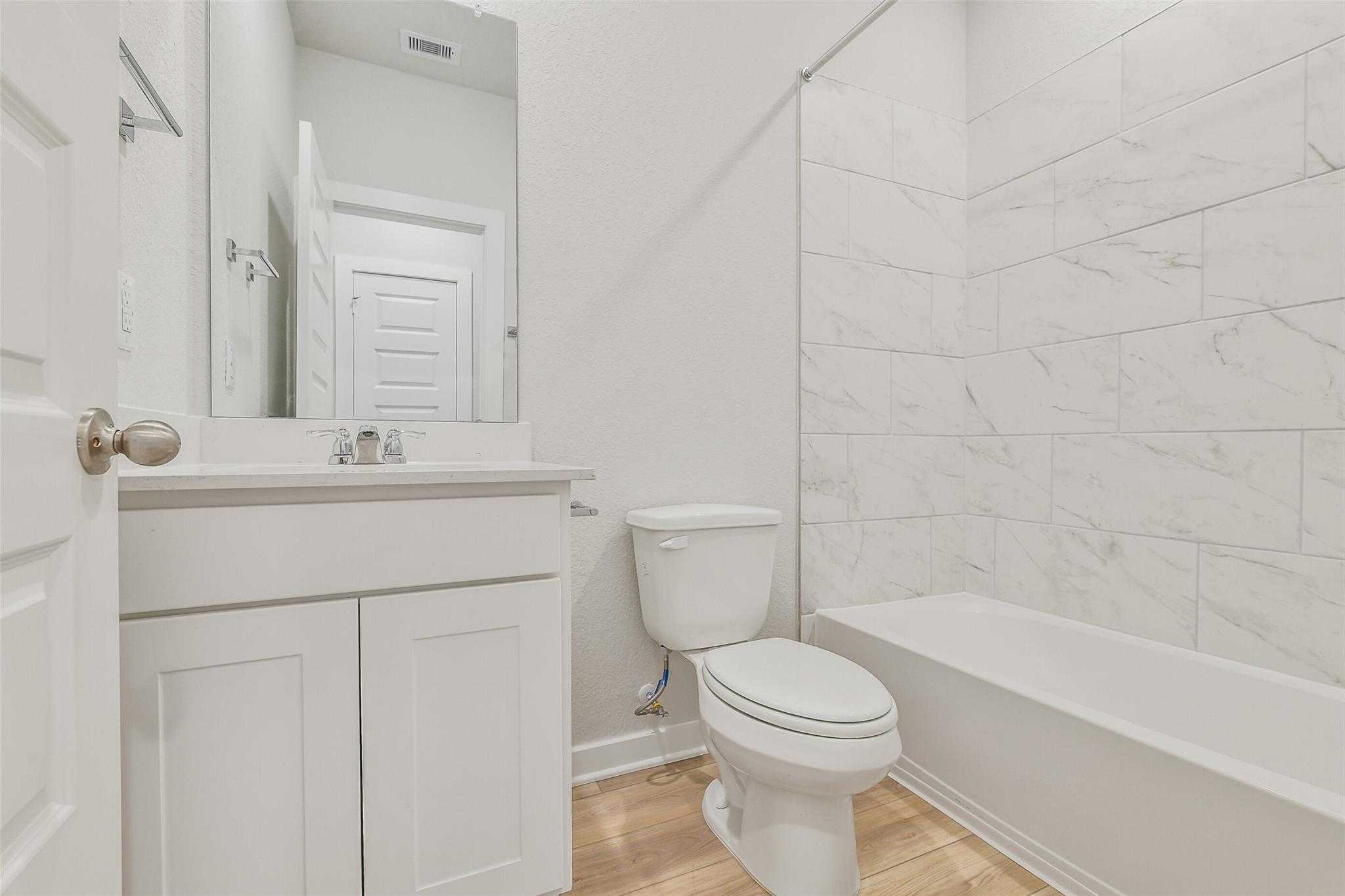 Bright bathroom with white subway tile shower, soaking tub, single vanity, and wood floors in Davidson Homes The Rio Grande H, Magnolia, Texas