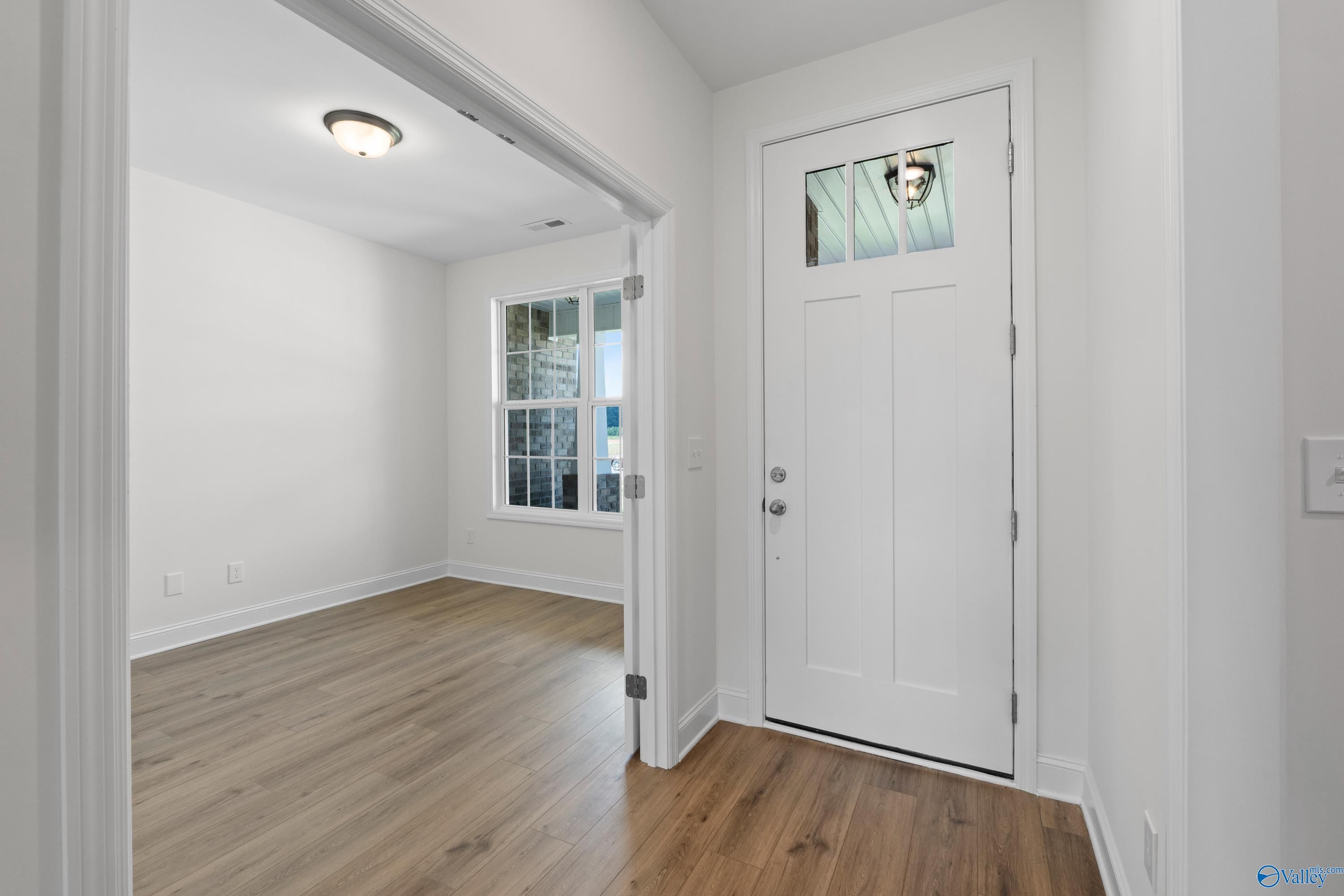 Bright entryway with white paneled front door, transom window, and oak hardwood floors in Davidson Homes The Rockford B, Toney, AL