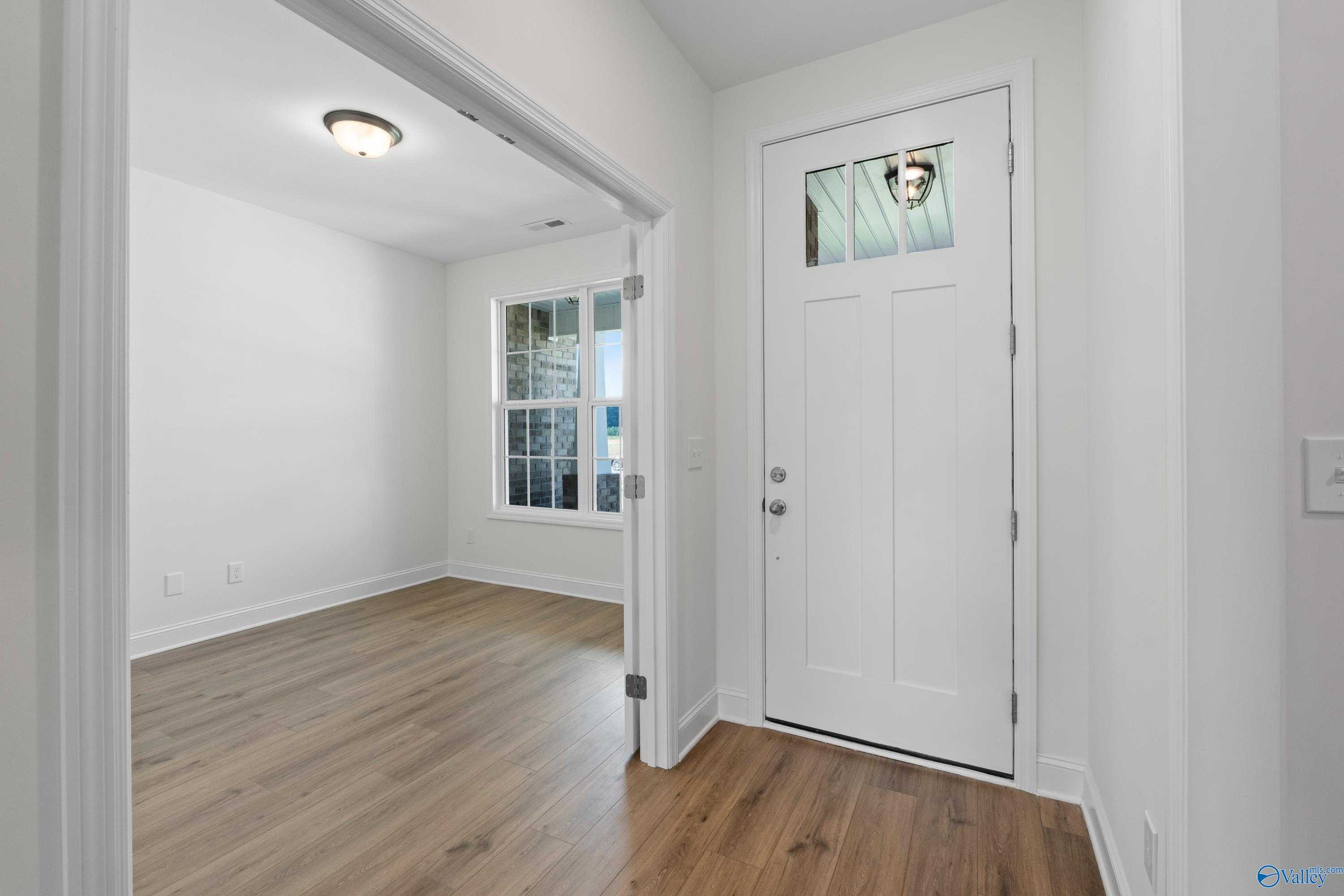 Bright entryway with white paneled front door, transom window, and oak hardwood floors in Davidson Homes The Rockford B, Toney, AL