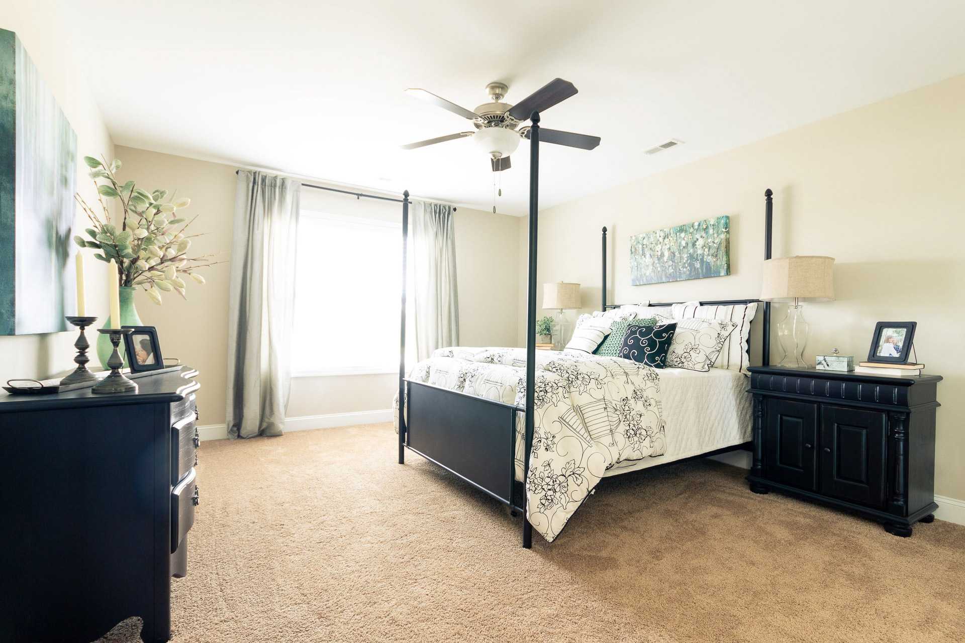 Spacious master bedroom at Summer Pointe in Madison, Alabama with king bed, ceiling fan, sheer curtains, and abstract wall art