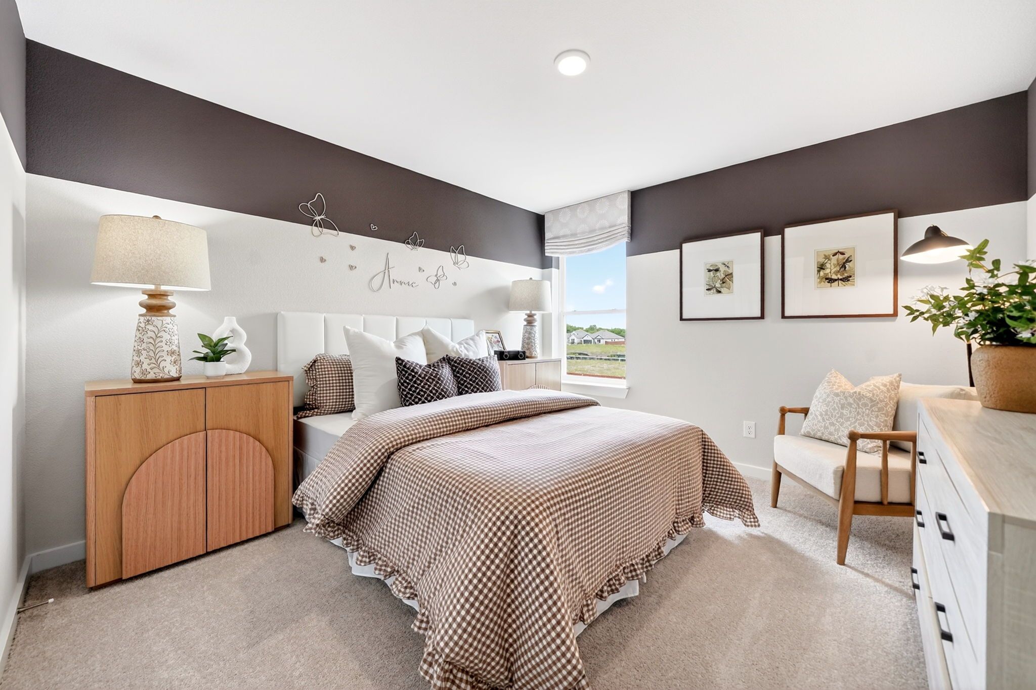 Cozy bedroom in Heartland Texas by Davidson Homes with checkered beige bedding, arched dresser, armchair, and window view