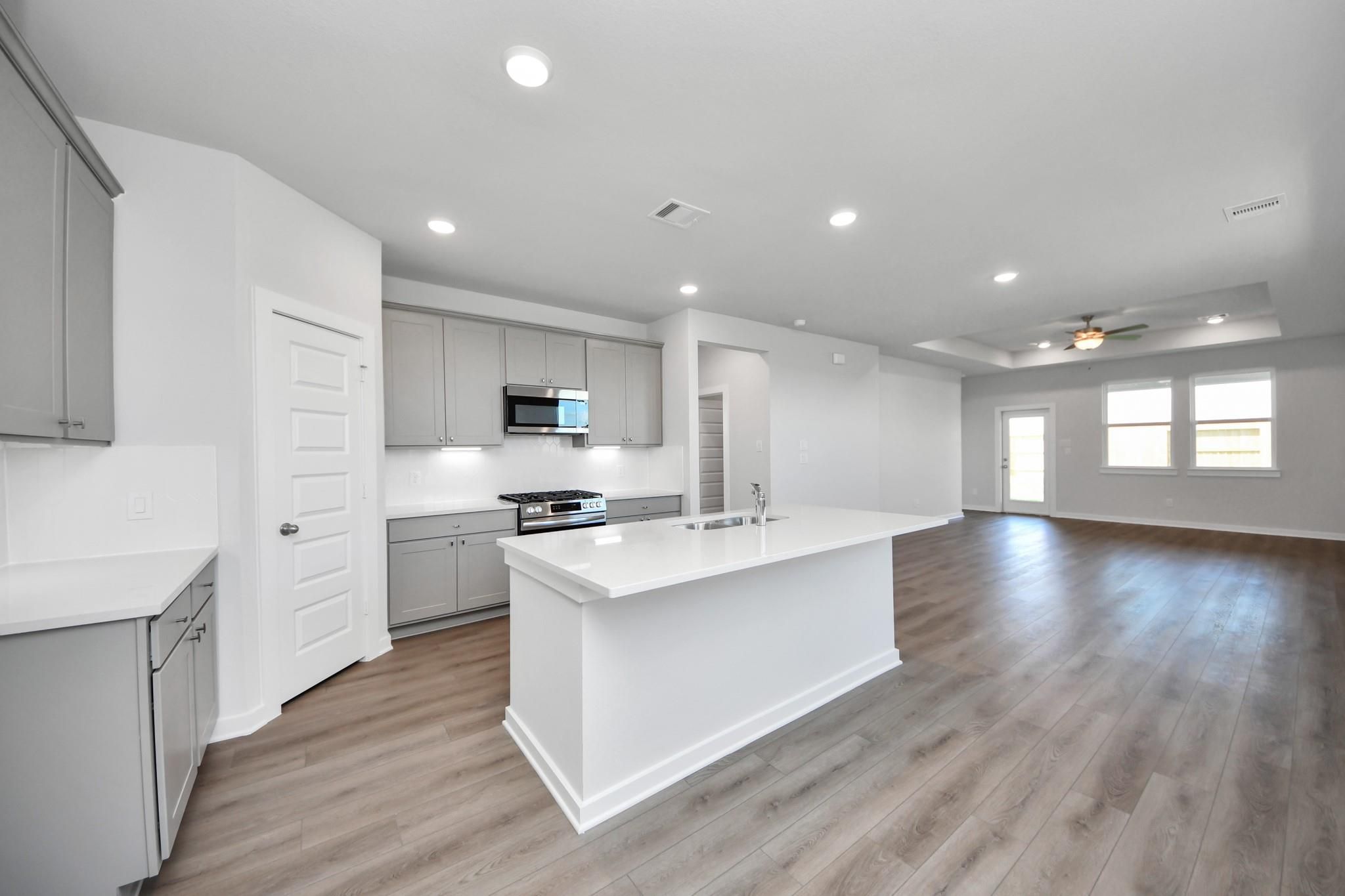 Open-concept kitchen with white quartz island and grey cabinetry in The Riviera A floor plan at Emberly, Beasley, Texas.