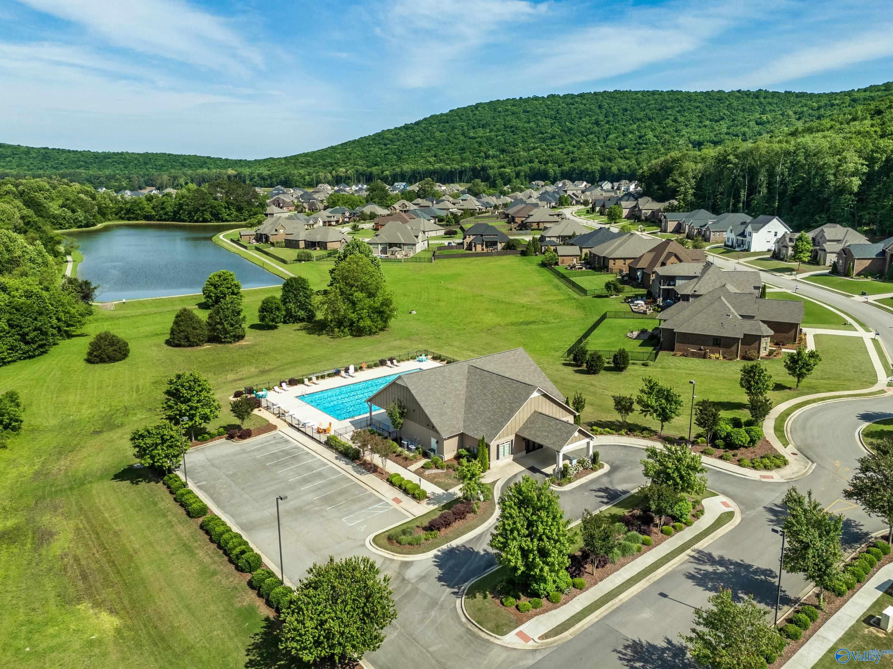 Aerial view of community pool and clubhouse surrounded by homes, lake and green hills in The Meadows at Hampton Cove, Owens Cross Roads, Alabama