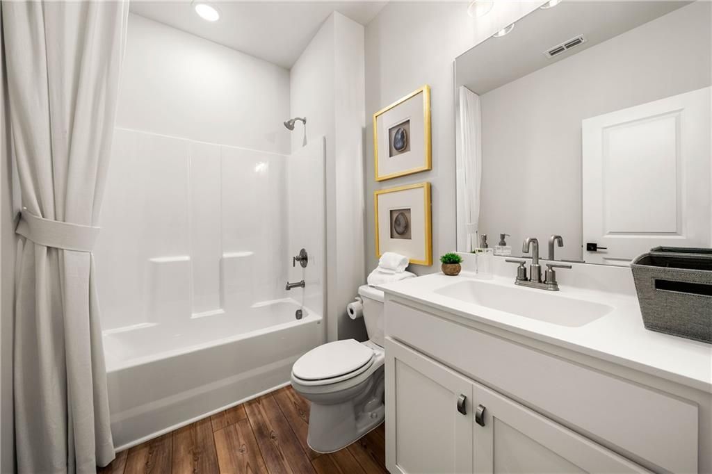Bright white bathroom with tub-shower combo, single vanity, framed art, and hardwood floors in Davidson Homes The Willow B, Riverwood, Dallas, GA