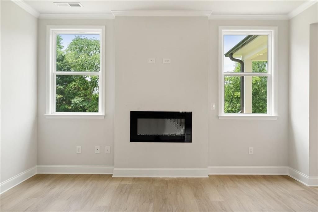 Modern living room with linear black fireplace, large windows overlooking trees, hardwood floors in The Willow D home at Wehunt Meadows, Hoschton