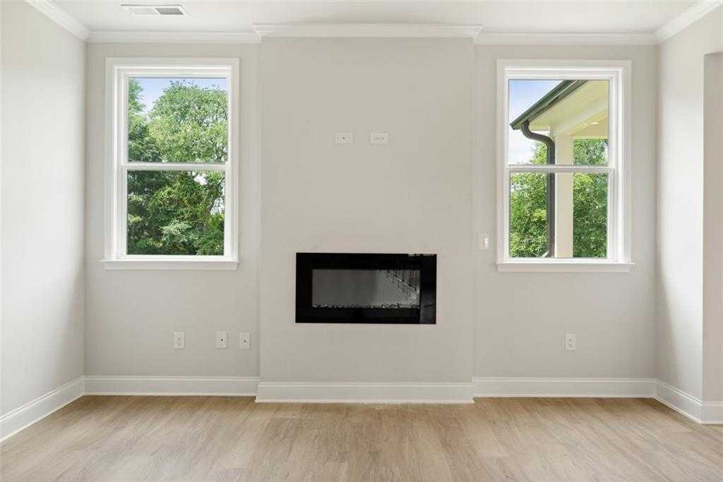 Modern living room with linear black fireplace, large windows overlooking trees, hardwood floors in The Willow D home at Wehunt Meadows, Hoschton
