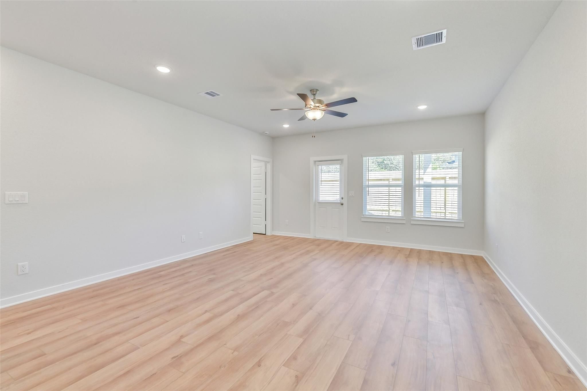 Spacious living room with light oak floors, ceiling fan, recessed lights, and large windows in Davidson Homes The Blanco E, Magnolia, Texas