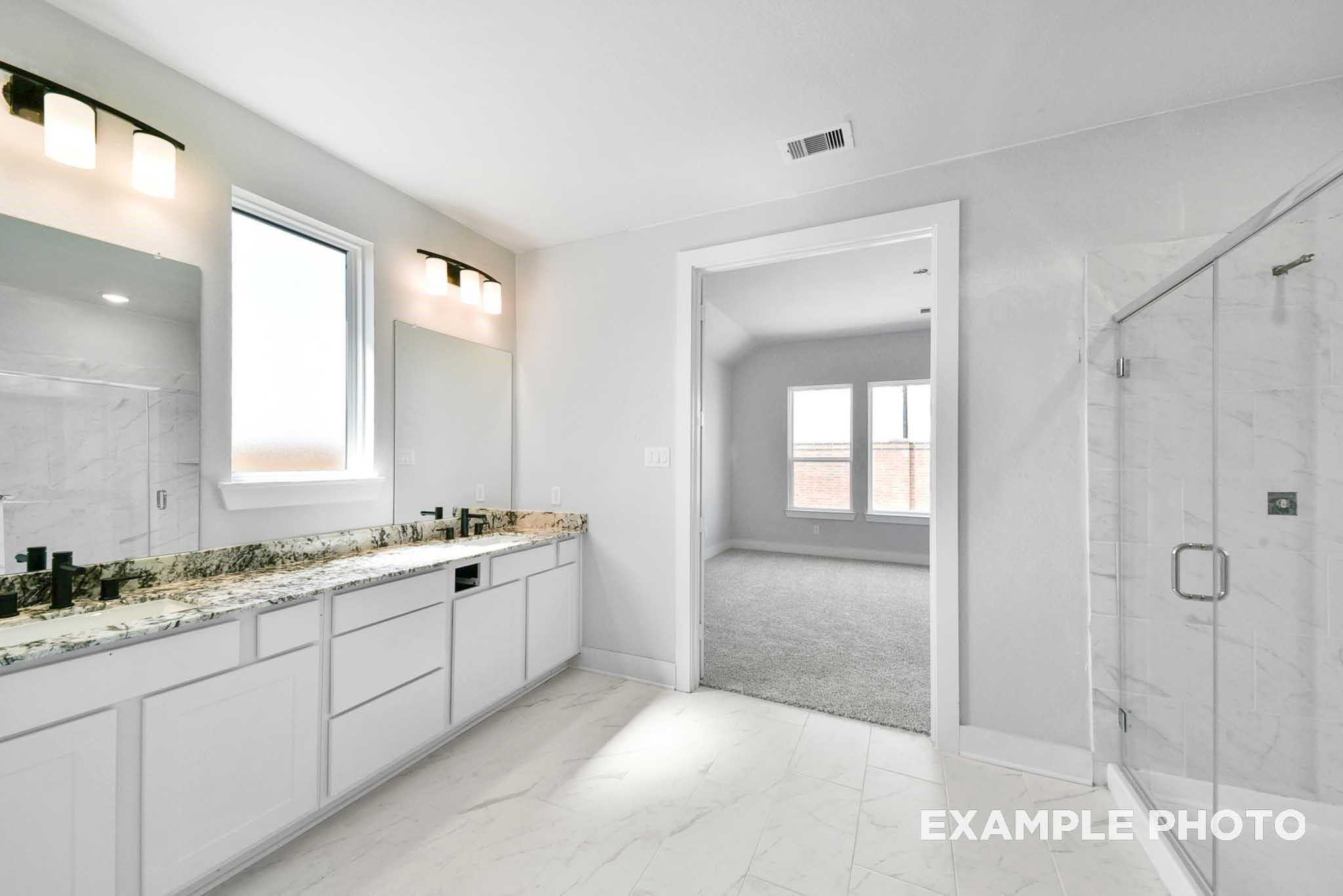 Modern master bathroom with double granite vanity, frameless glass shower, and bedroom view in Davidson Homes The George A, Texas City