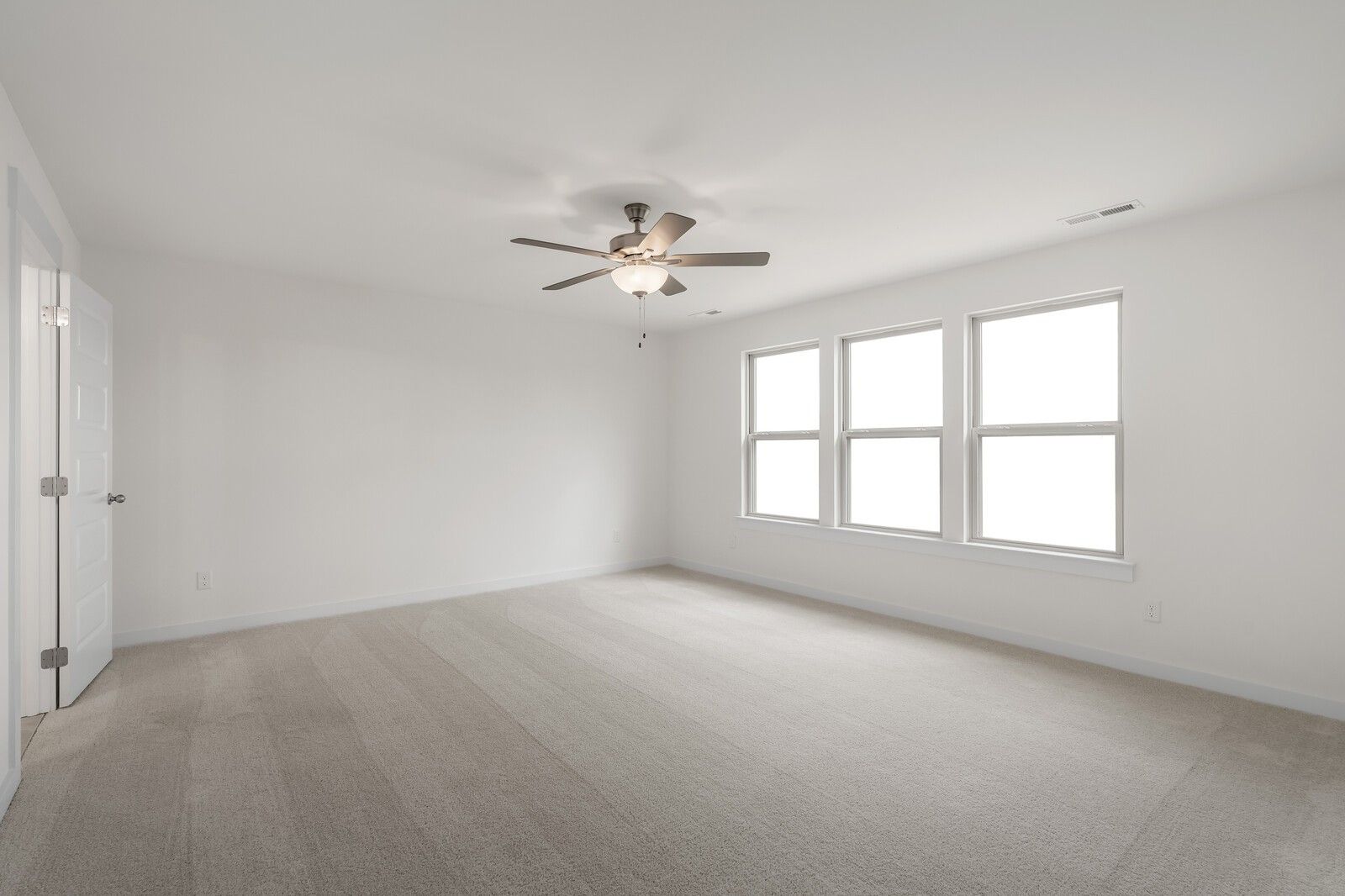 Spacious empty bedroom with three large windows, ceiling fan, and carpeted floor in Davidson Homes The Willow C, Gallatin, TN