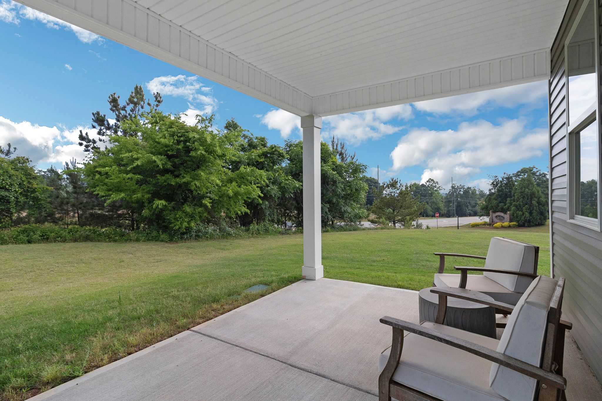 Covered back porch at Ivy Glen in Perry, Georgia featuring cushioned chairs, round table, concrete patio, lush green lawn, and tree views