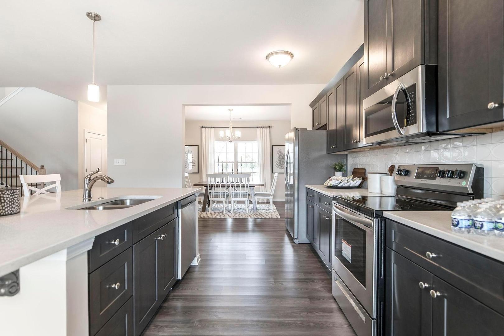 Spacious open-concept kitchen at Cape Reserve at Donahue Ridge in Auburn, Alabama with dark cabinets, white quartz counters, and stainless steel appliances
