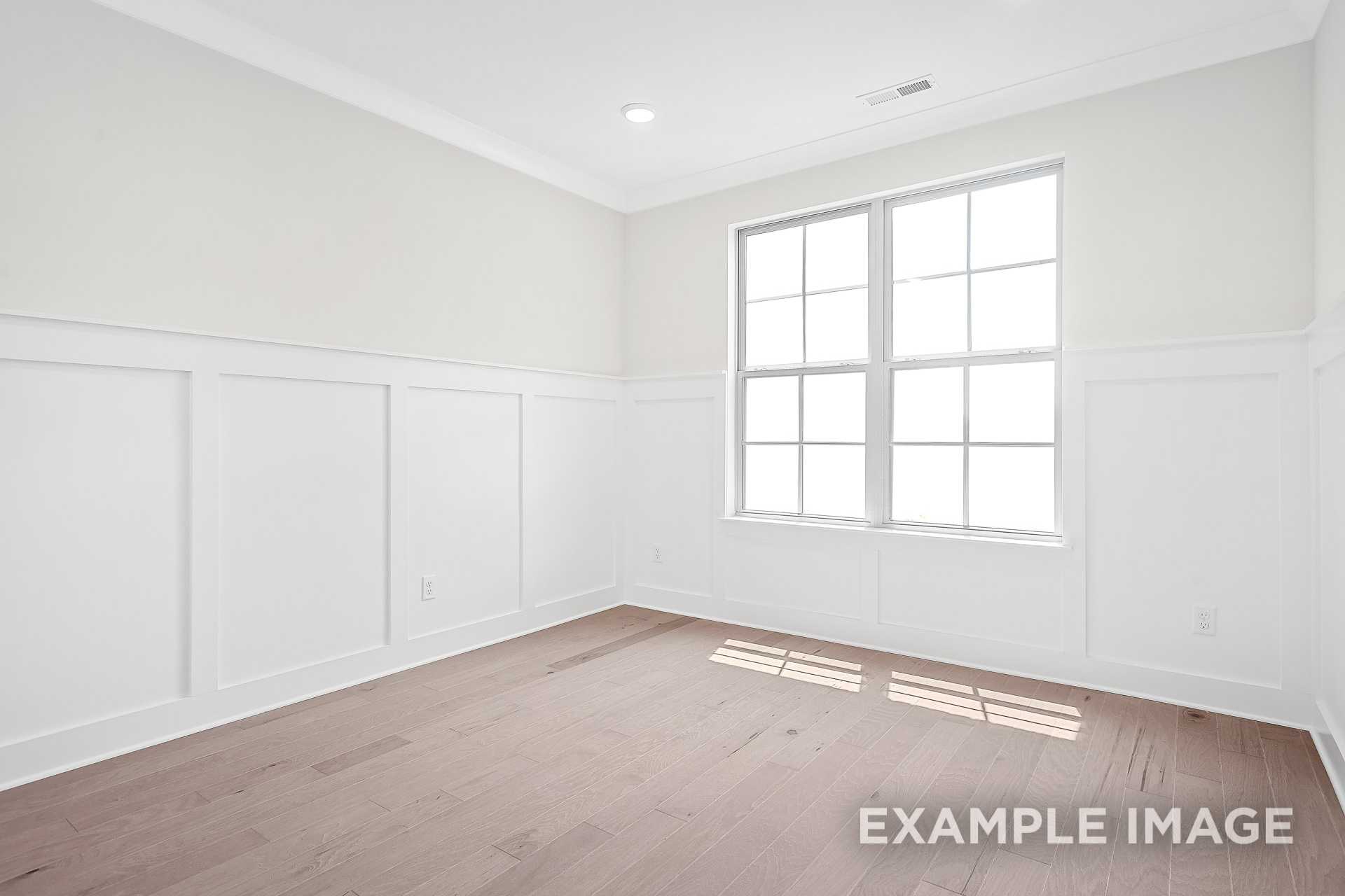 Bright empty bedroom in The Hawkins with white wainscoting, large double windows, and hardwood floors by Davidson Homes