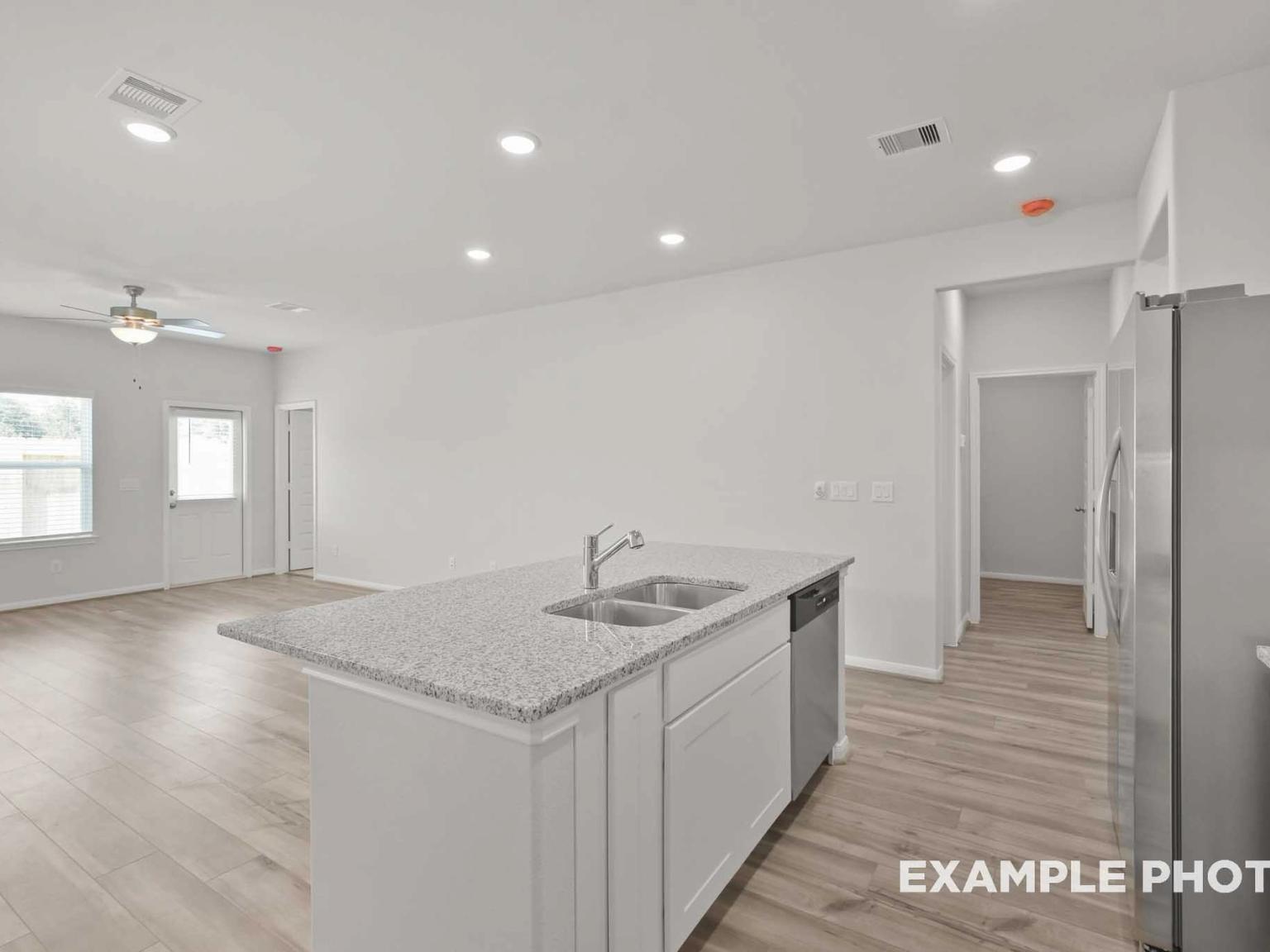 Modern open-concept kitchen with white island, granite counters, stainless fridge in Davidson Homes The Comal F, Conroe, TX