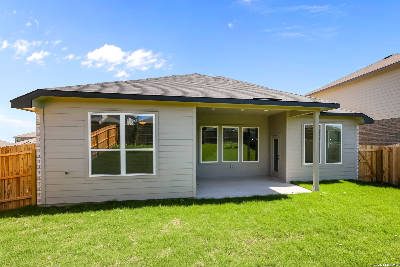 Rear view of modern two-story Sequoia B home with covered patio, large windows, and lush green backyard in Comanche Ridge, San Antonio