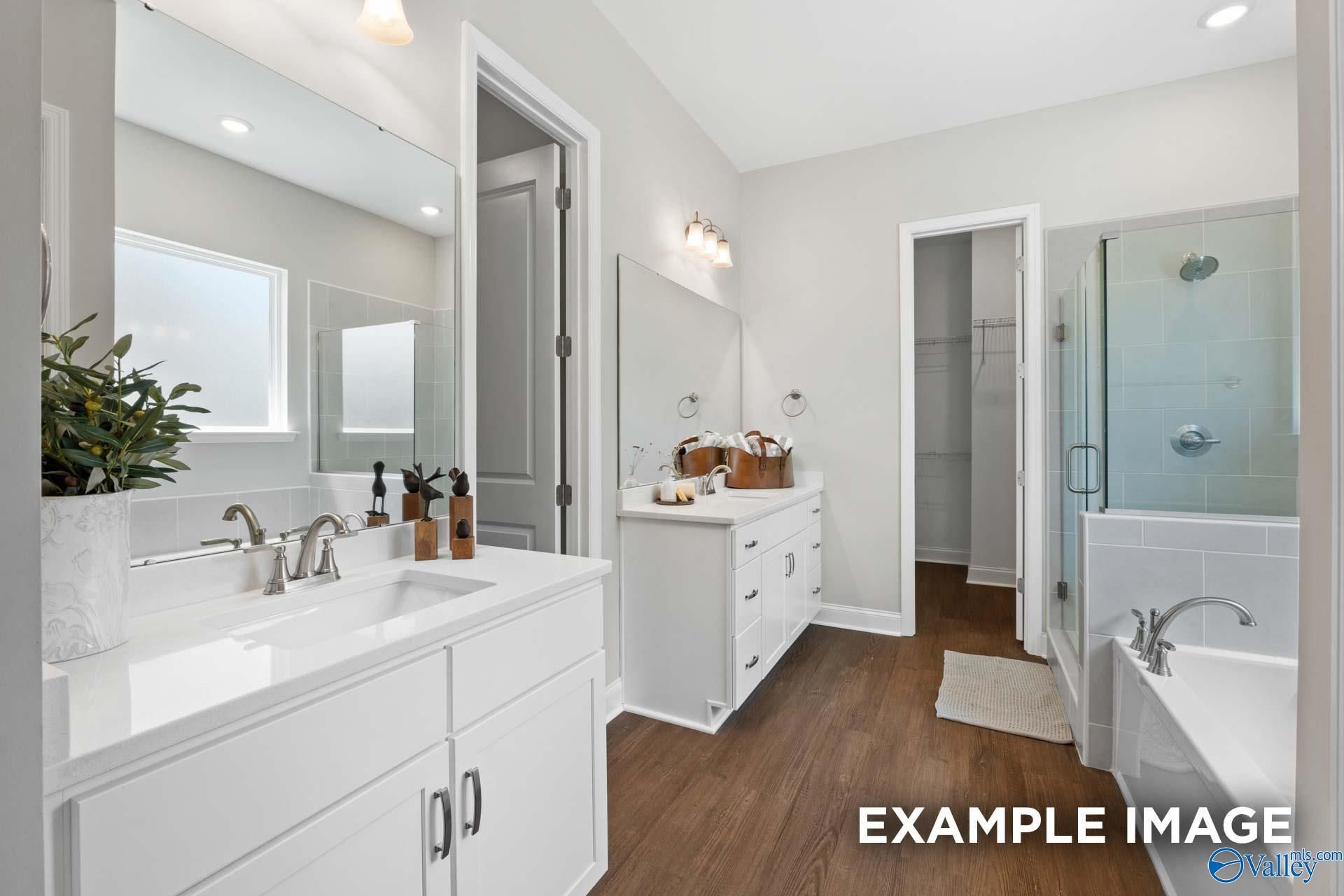 Elegant master bathroom featuring double white vanity, quartz counters, glass shower, and soaking tub in Evermore Homes The Haven E