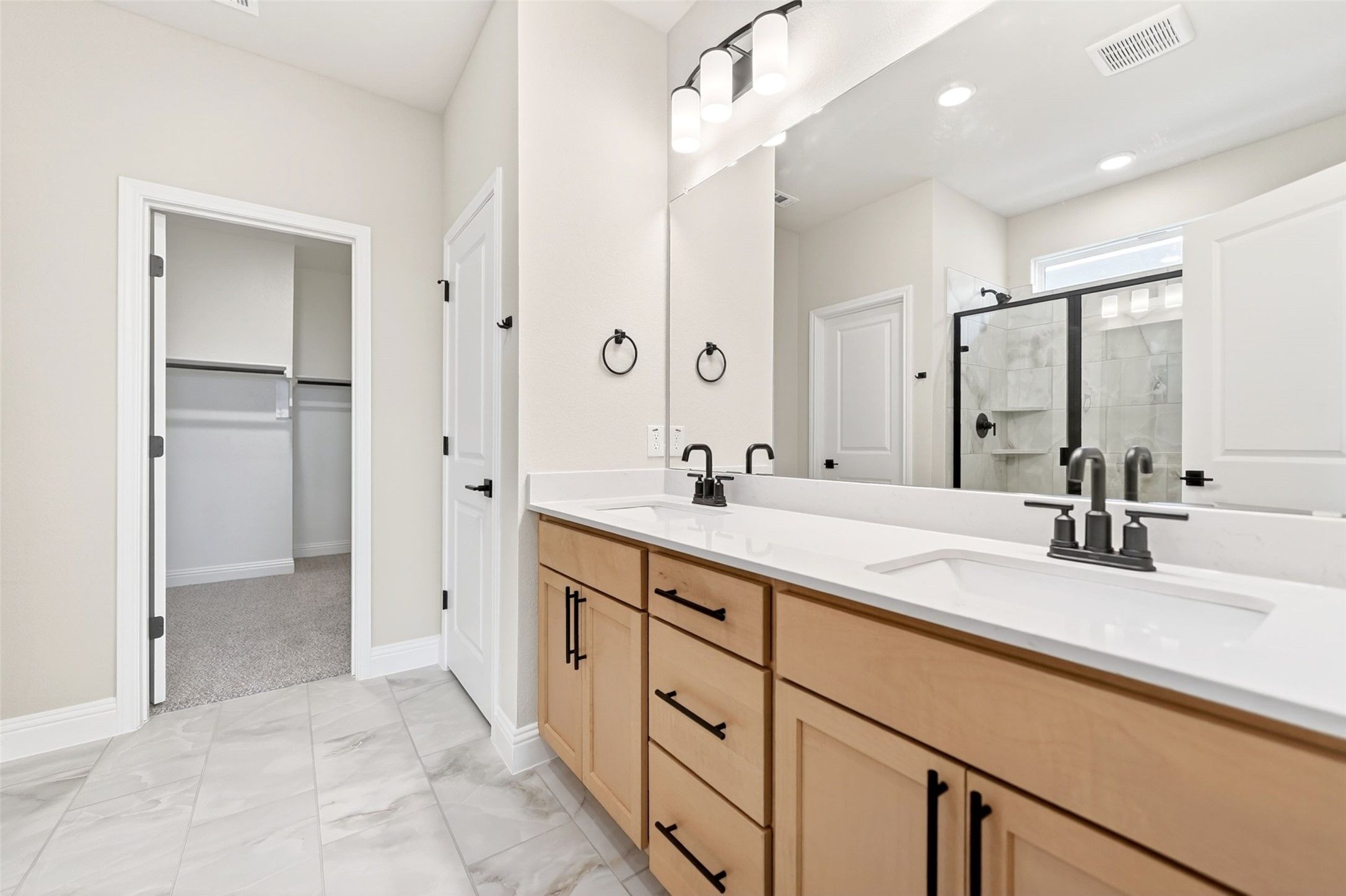 Modern primary bathroom with double vanity, light wood cabinets, and walk-in closet in The Holly C floor plan, Anna, TX.