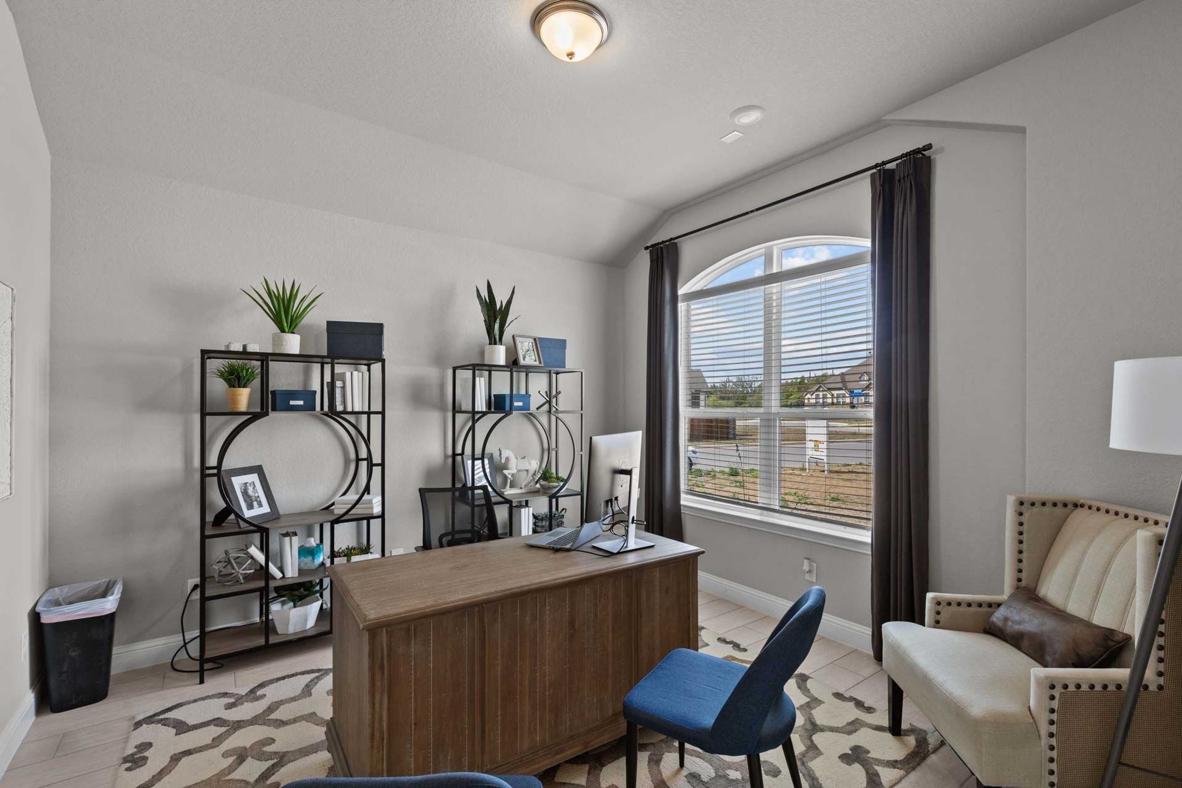 Contemporary home office in Ladera San Antonio with wooden desk, bookshelves, plants, blue chair, and arched window