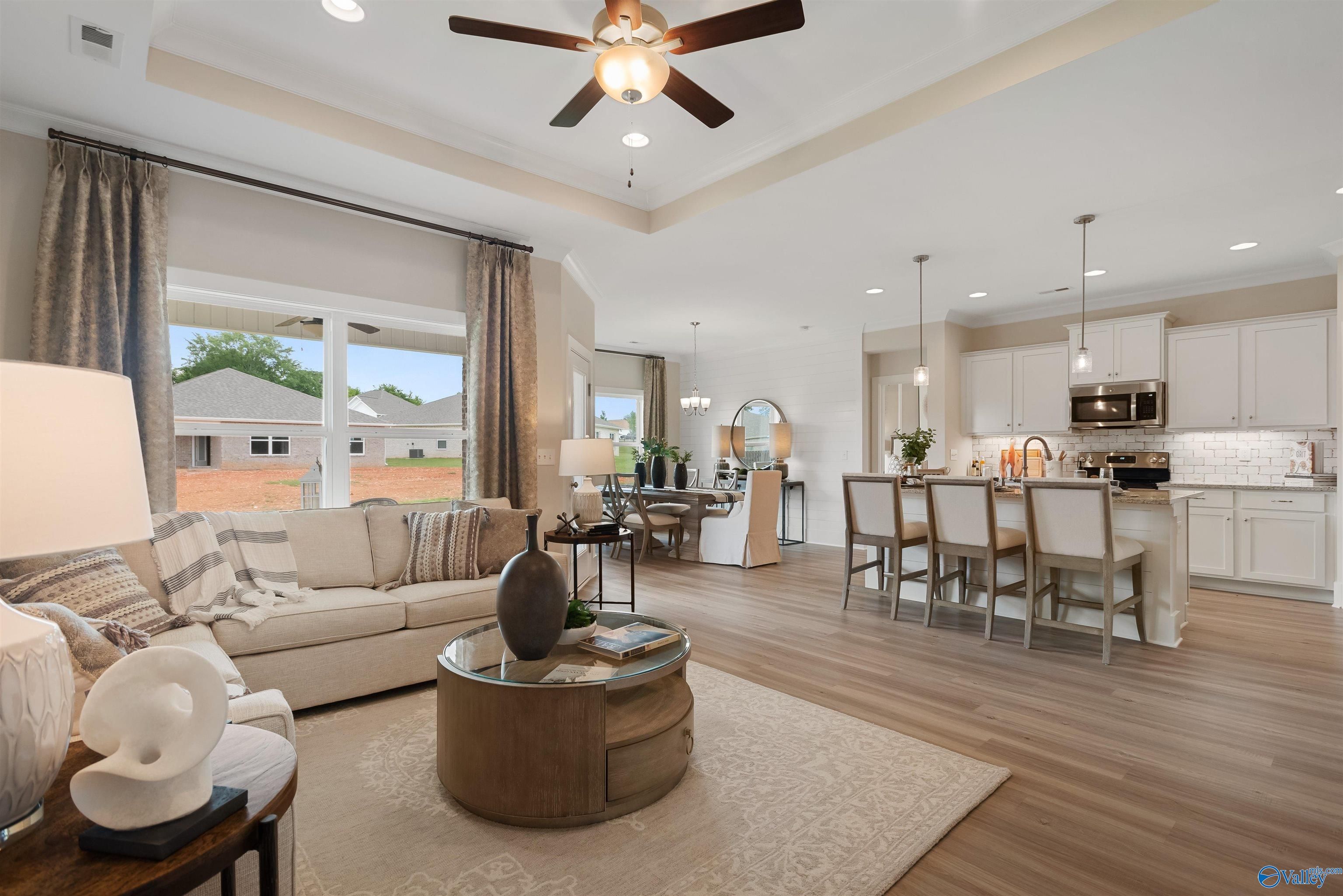 Open-concept living room with beige sofa, wooden coffee table, and kitchen island in Davidson Homes The Everett, New Market, Alabama