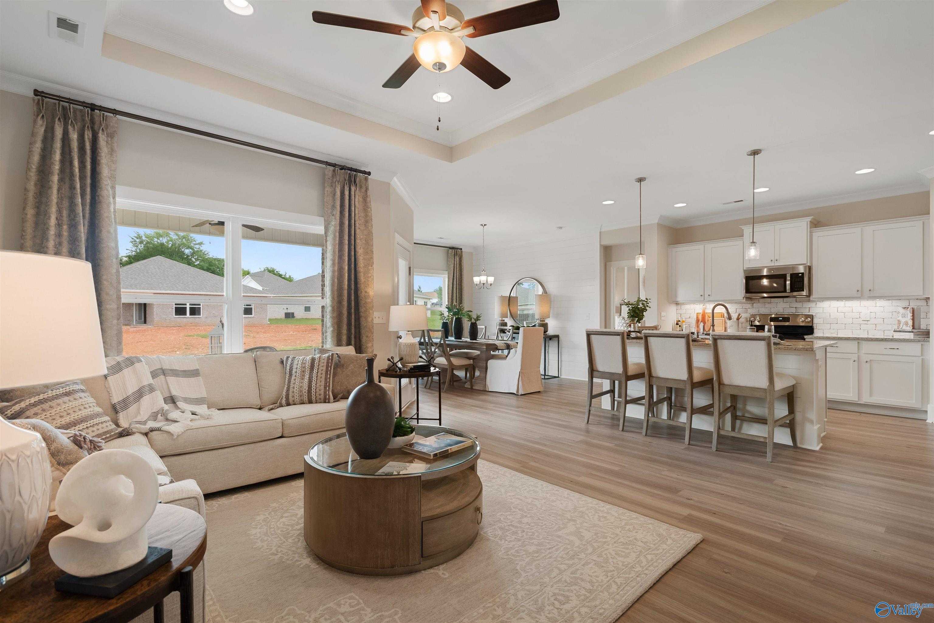 Open-concept living room with beige sofa, wooden coffee table, and kitchen island in Davidson Homes The Everett, New Market, Alabama