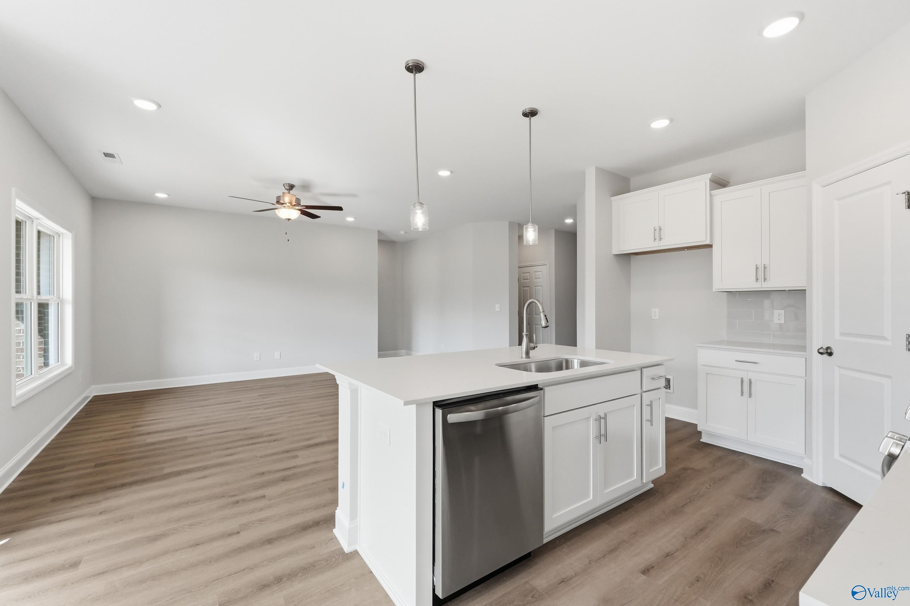 Modern open-concept kitchen with white quartz island, stainless sink, and ceiling fan in The Asheville C home, Huntsville, AL