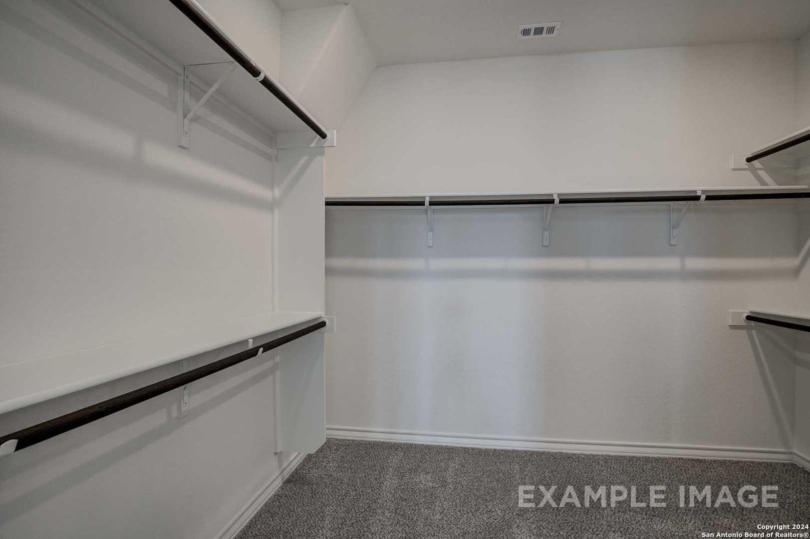 Spacious walk-in closet with built-in dark wood shelving and carpeted floor in Davidson Homes The Garner C, Castroville, Texas