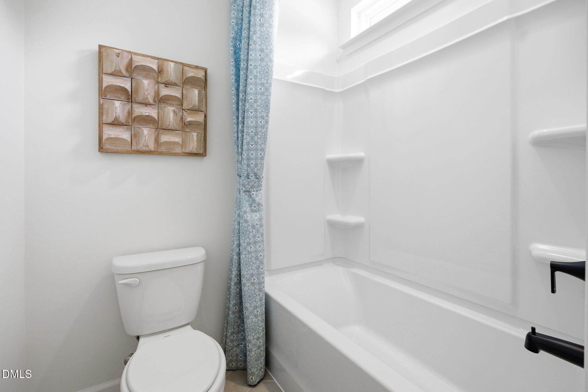 Full bathroom with white tub-shower combo and blue patterned curtain in The Ashport M at Wendell Ridge, North Carolina.