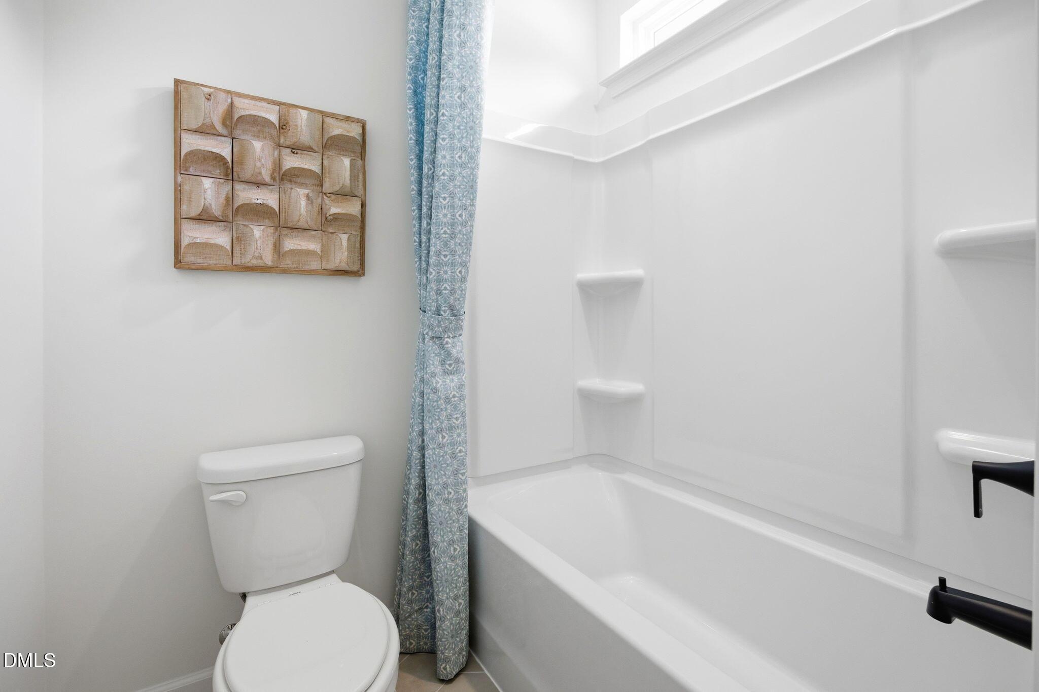 Full bathroom with white tub-shower combo and blue patterned curtain in The Ashport M at Wendell Ridge, North Carolina.