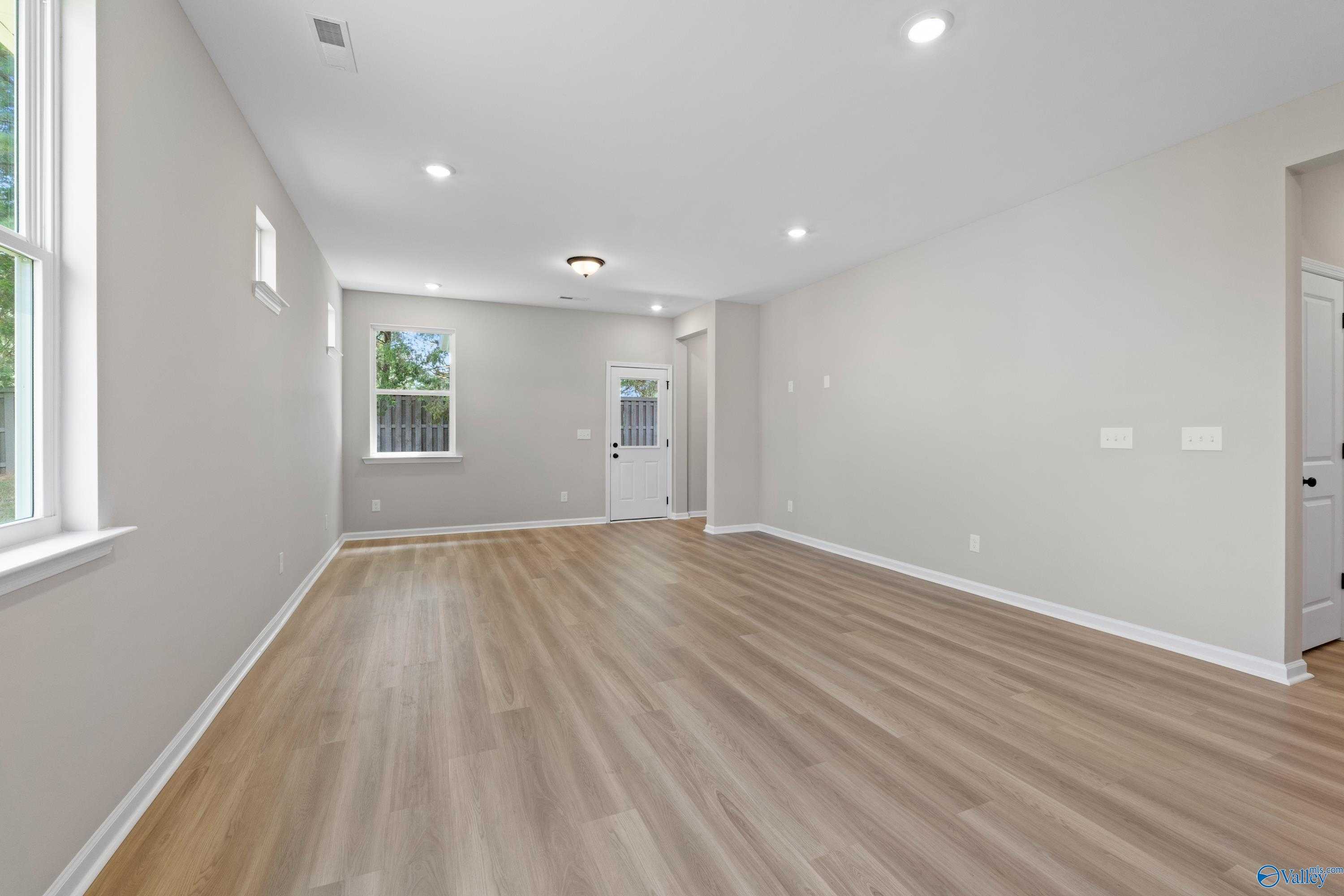 Bright empty living room with light gray walls, luxury vinyl plank floors, large windows, and recessed lighting in The Nantucket by Evermore Homes, Madison AL