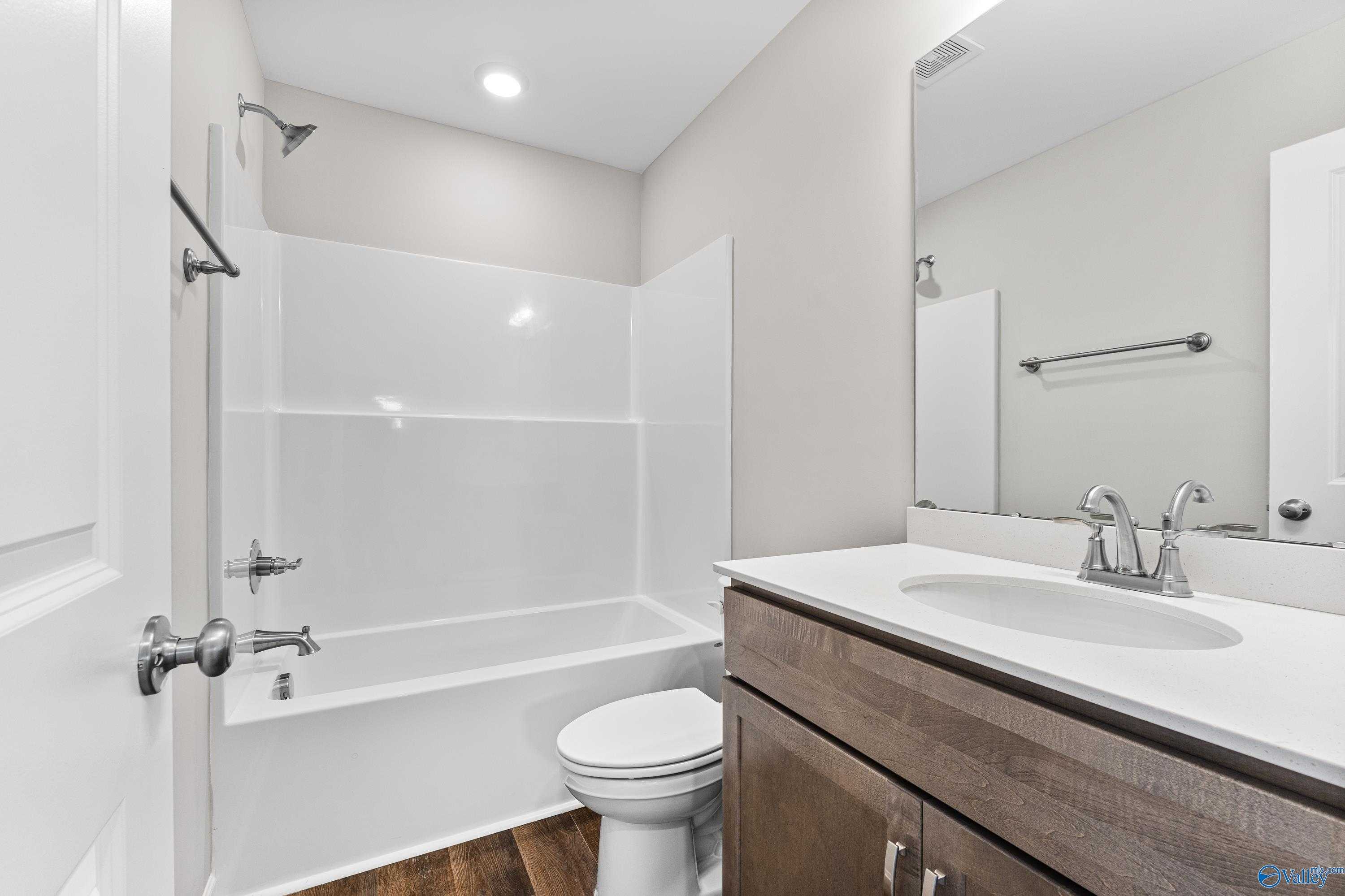 Modern bathroom with white tub-shower combo, wooden vanity sink, mirror, and toilet in Davidson Homes The Haven, Huntsville, Alabama