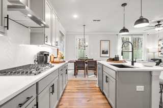 Open-concept kitchen in The Washington H townhome: white shaker cabinets, gray island with farmhouse sink, subway tile backsplash, hardwood floors, dining nook