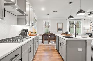Open-concept kitchen in The Washington H townhome: white shaker cabinets, gray island with farmhouse sink, subway tile backsplash, hardwood floors, dining nook