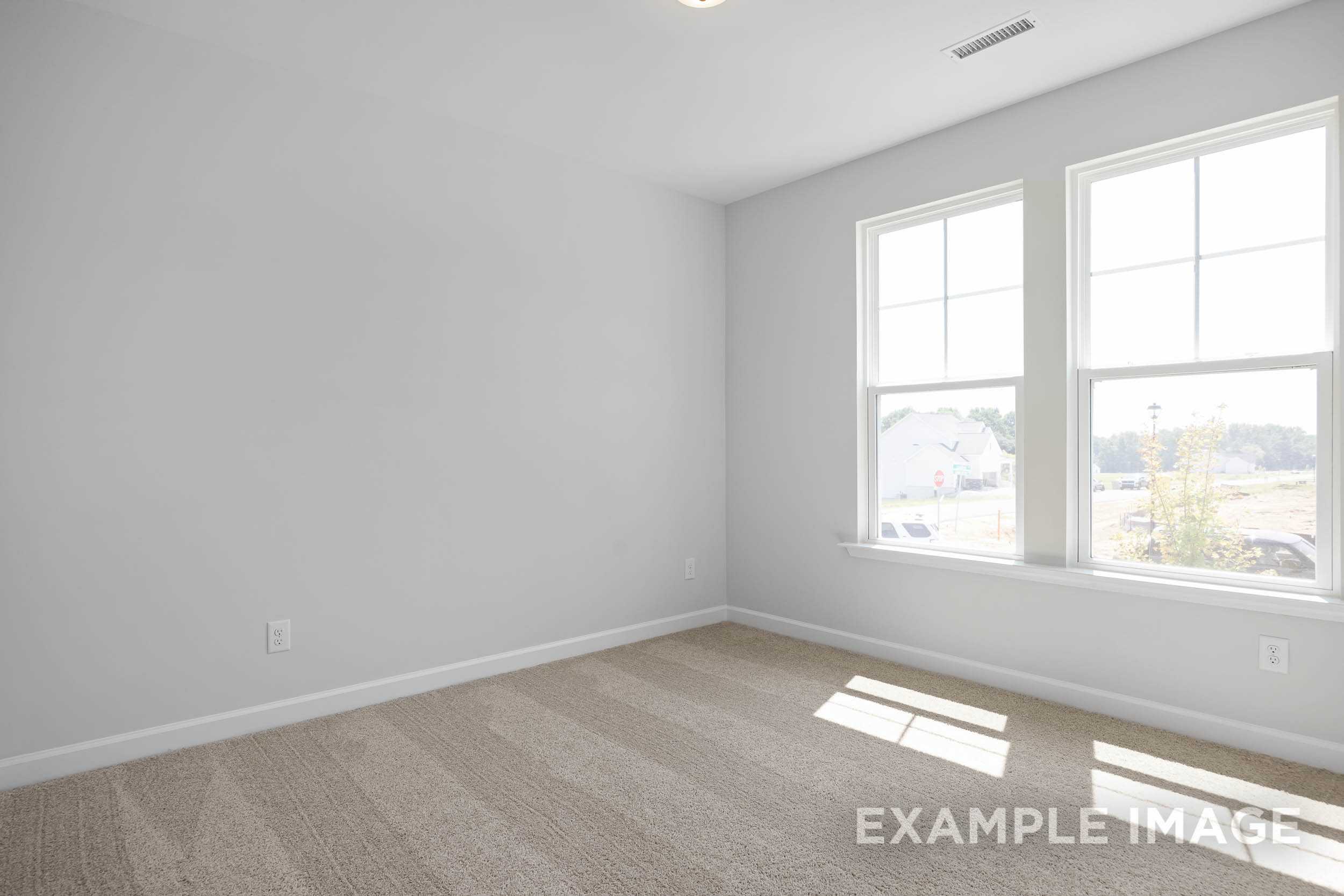 Spacious empty bedroom in The Daphne C by Davidson Homes, Lillington NC, with light gray walls, large sunny windows, beige carpet