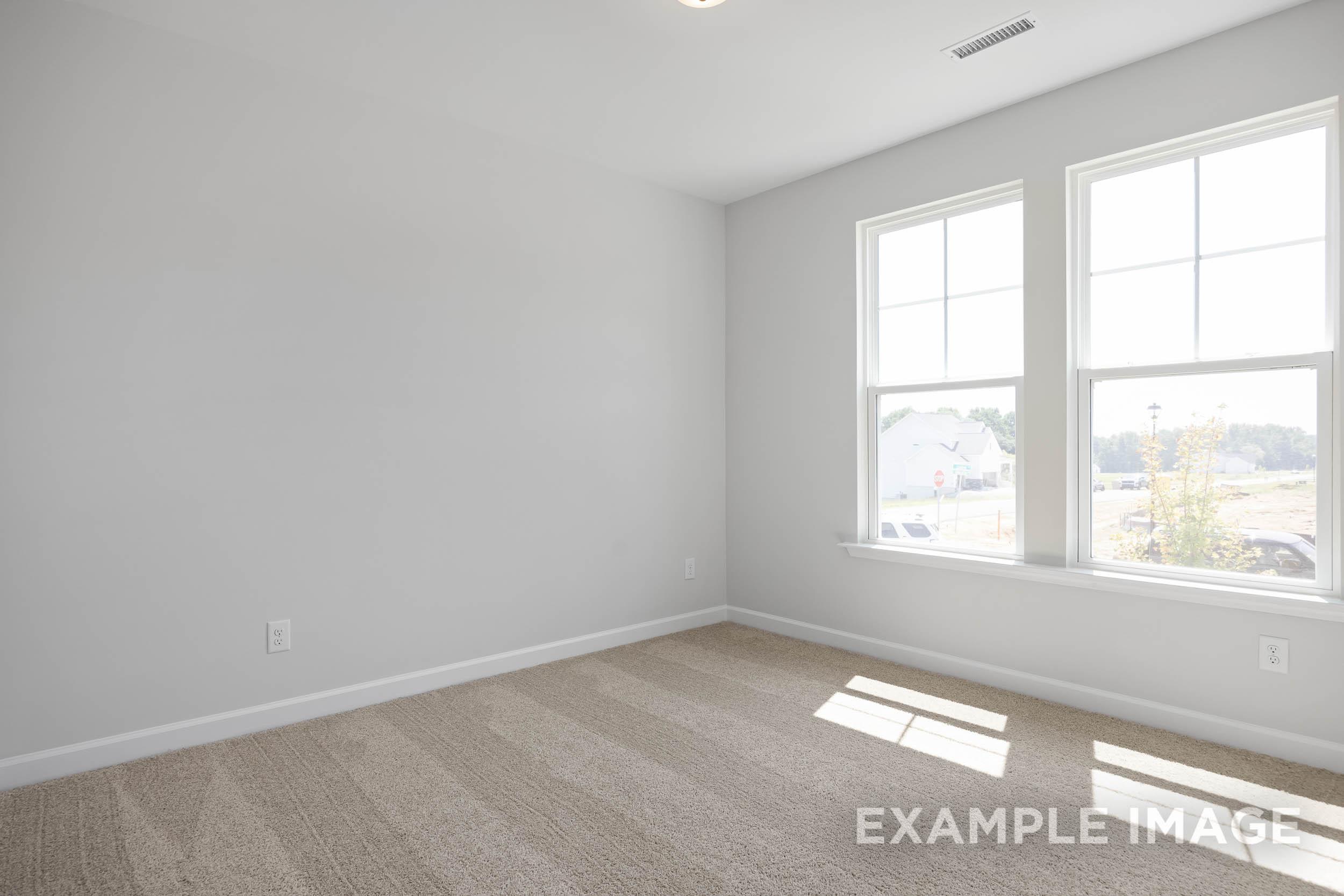 Spacious empty bedroom in The Daphne C by Davidson Homes, Lillington NC, with light gray walls, large sunny windows, beige carpet