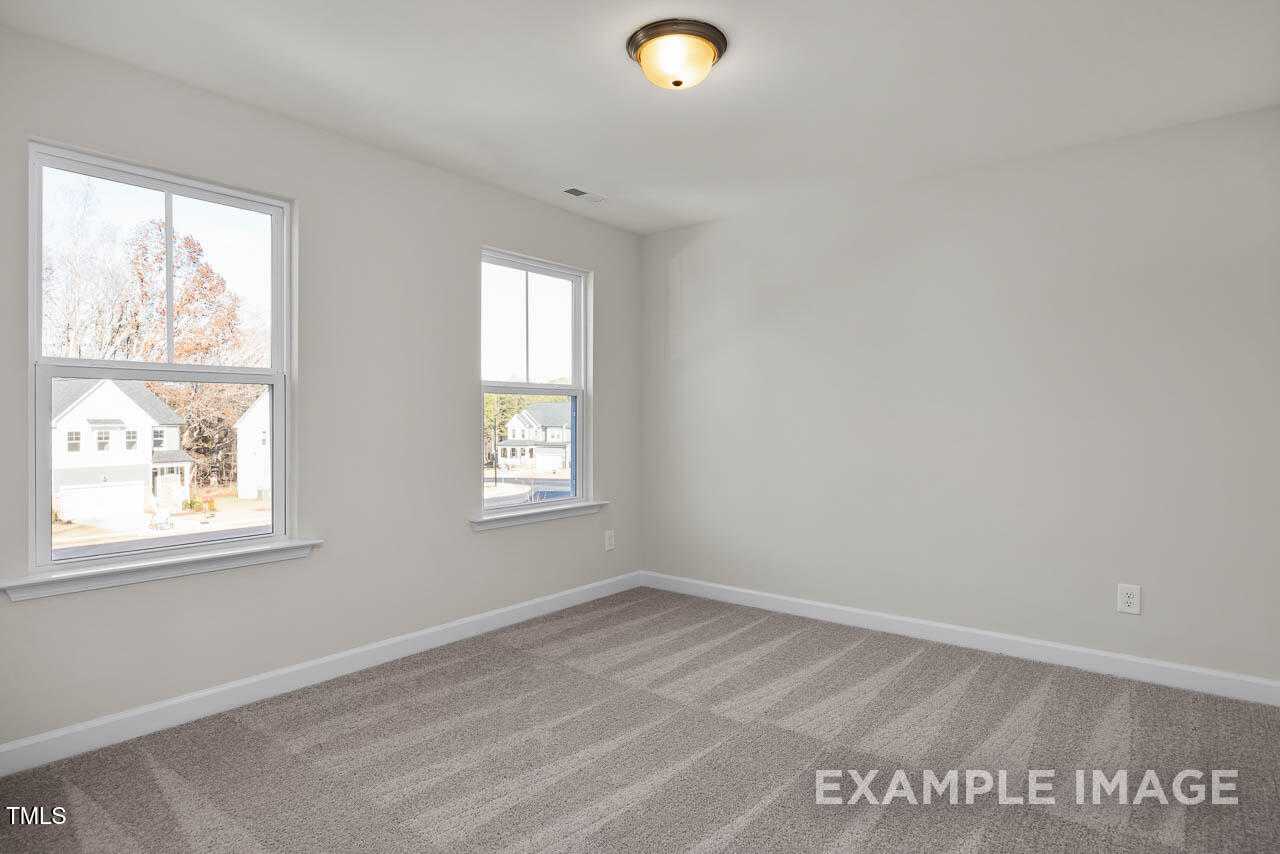 Bright empty bedroom with large windows overlooking autumn trees and beige carpet in The Hickory II B, Lillington, NC