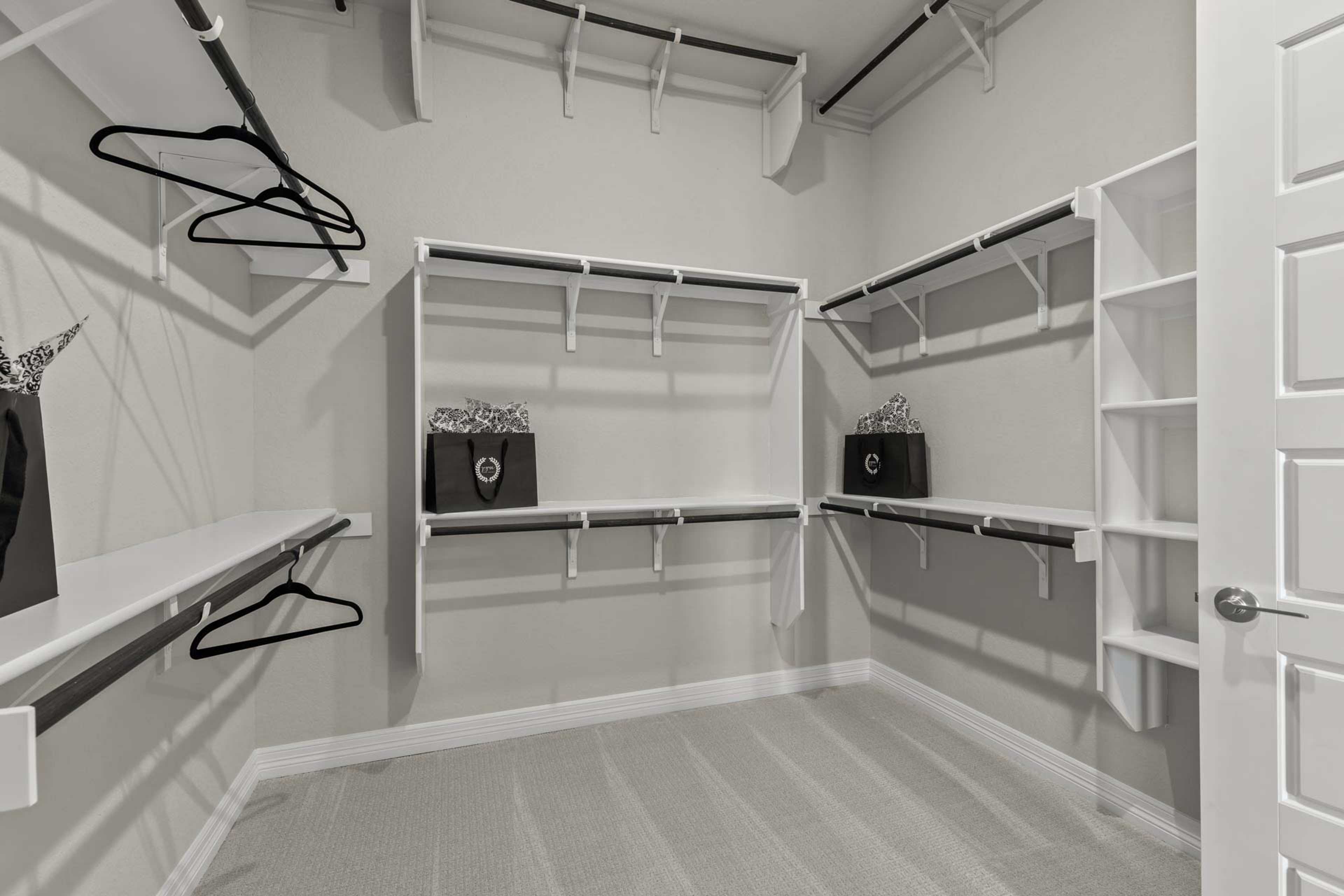 Spacious walk-in closet at Potranco Oaks in Castroville Texas by Davidson Homes with white built-in shelves hanging rods and purses