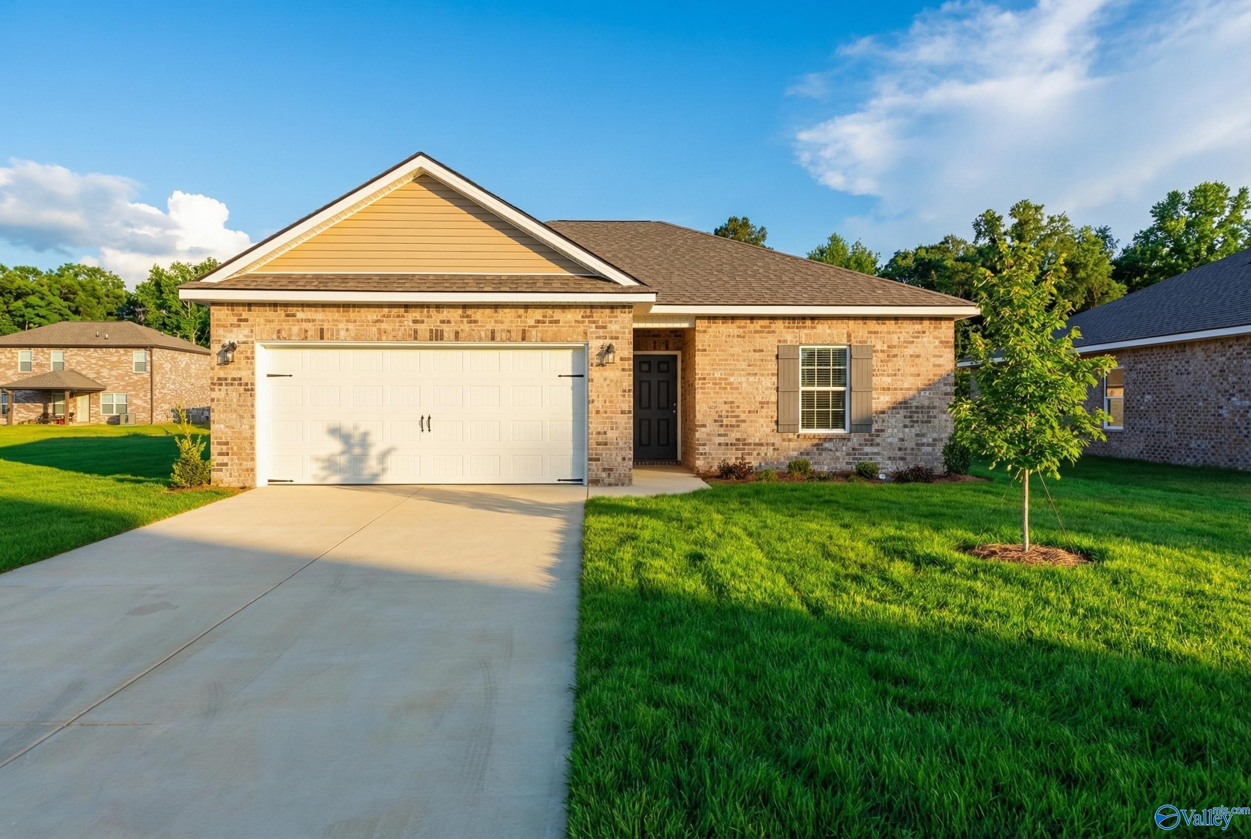 Modern 1-story 3-bedroom home with 2-car garage, brick accents, and lush green yard in Wood Trail, Toney, Alabama