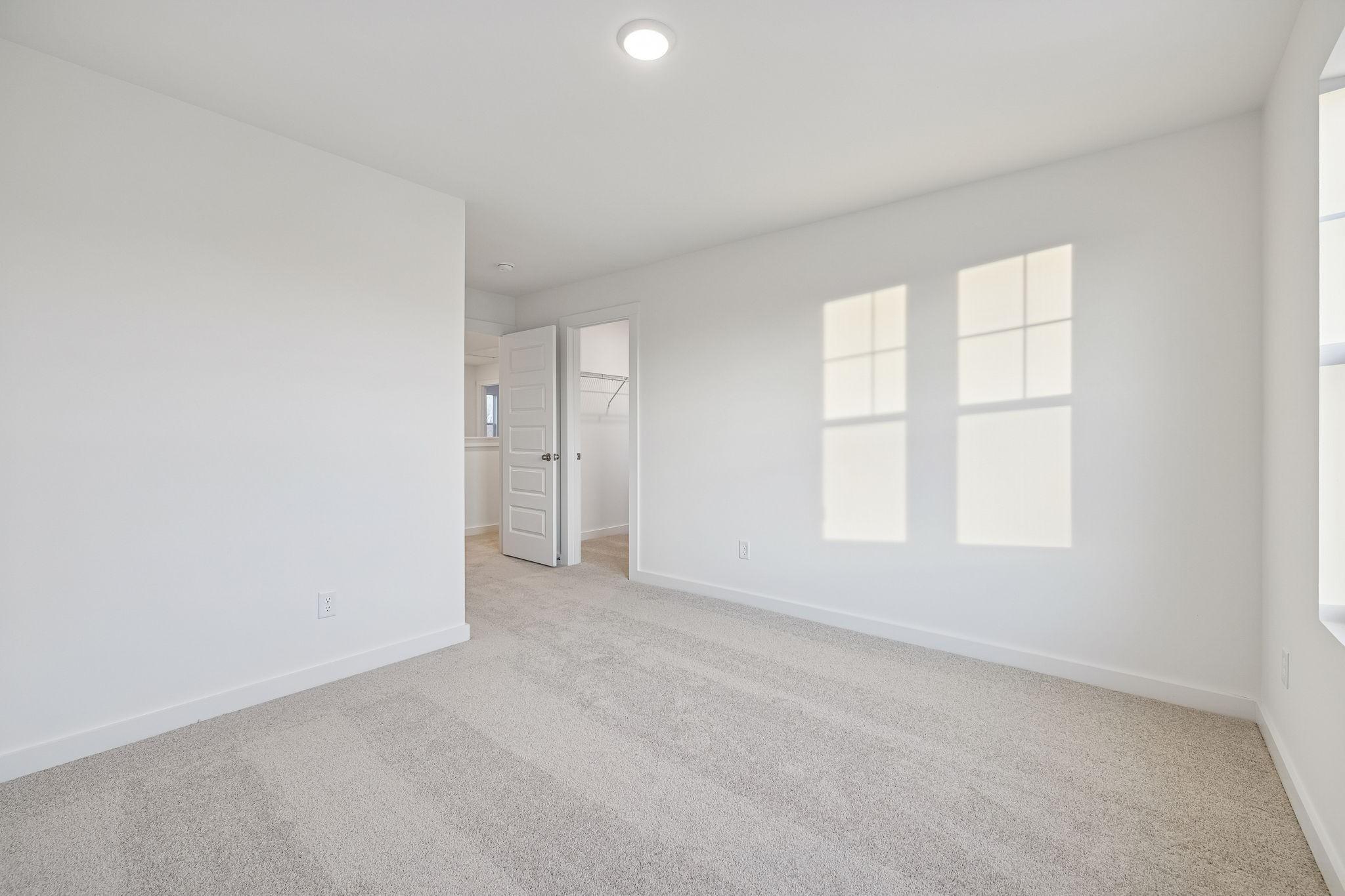 Bright empty bedroom with white walls, beige carpet, open walk-in closet, and sunlit windows in Davidson Homes The Willow, White House, TN