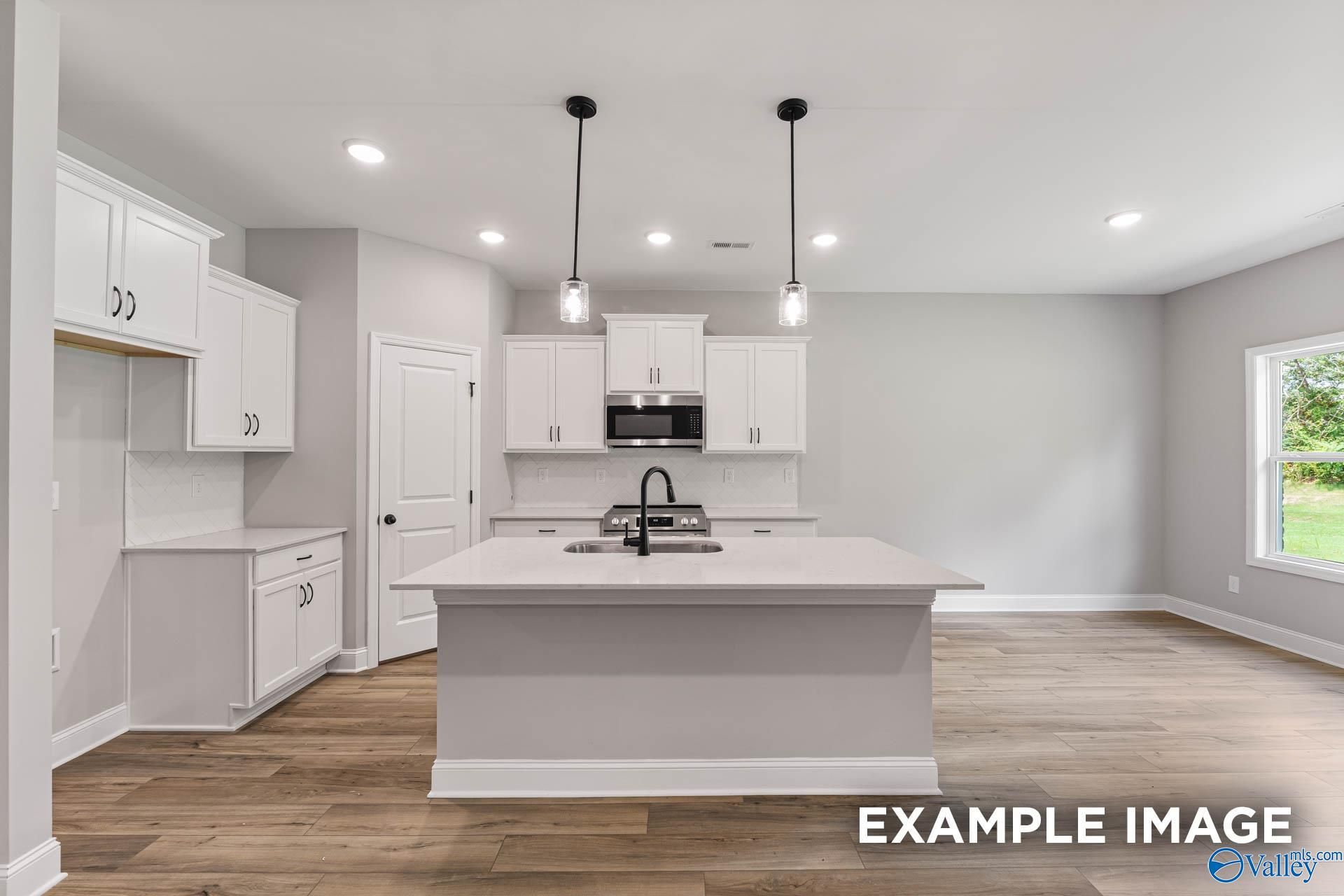 Modern white kitchen island with sink, pendant lights, and hardwood floors in The Asheville C floor plan, Hazel Green, AL
