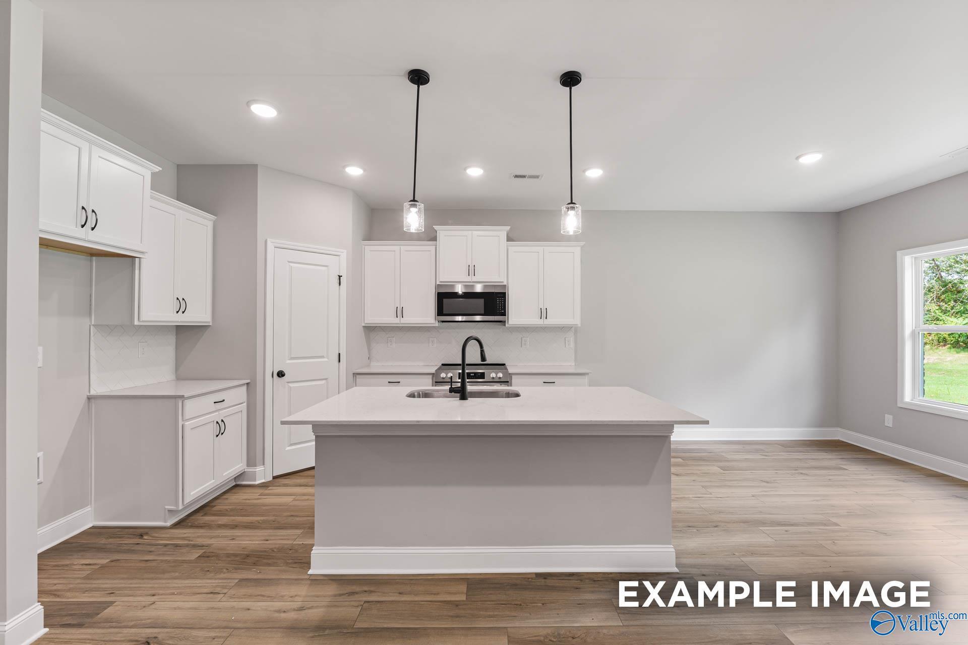 Modern white kitchen island with sink, pendant lights, and hardwood floors in The Asheville C floor plan, Hazel Green, AL