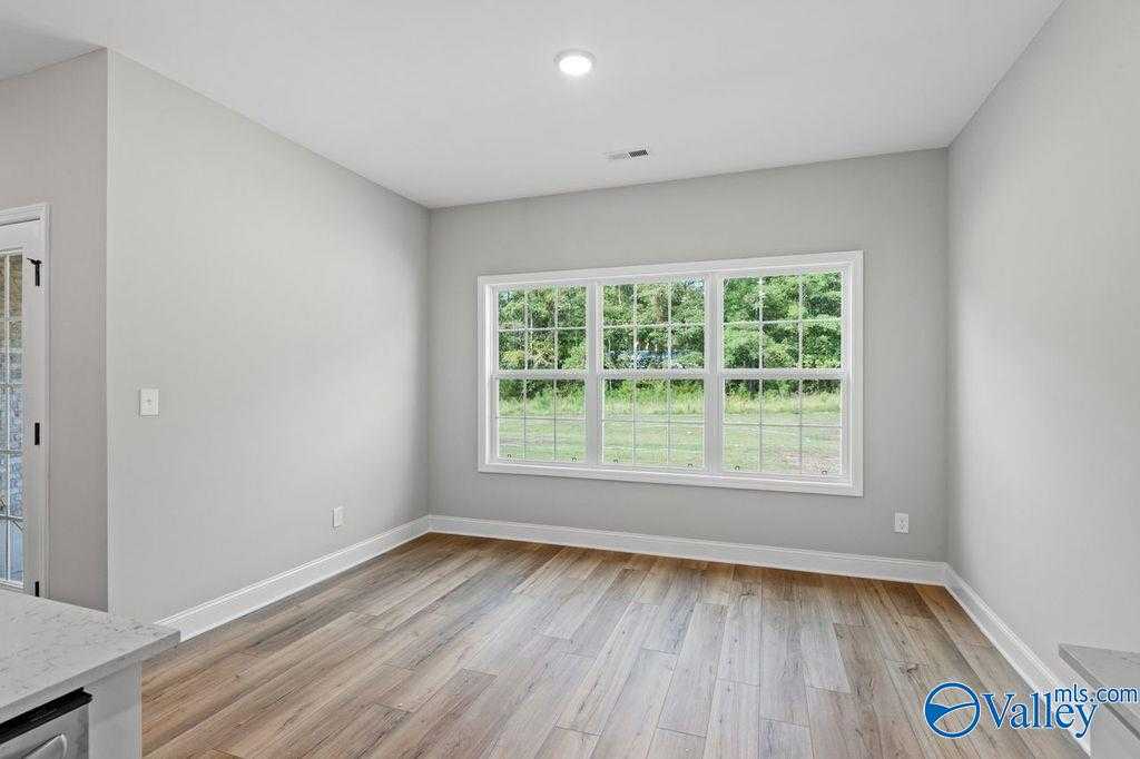 Bright empty room with large triple window overlooking green yard, gray walls, hardwood floors in Davidson Homes The Montgomery B, Hartselle, AL