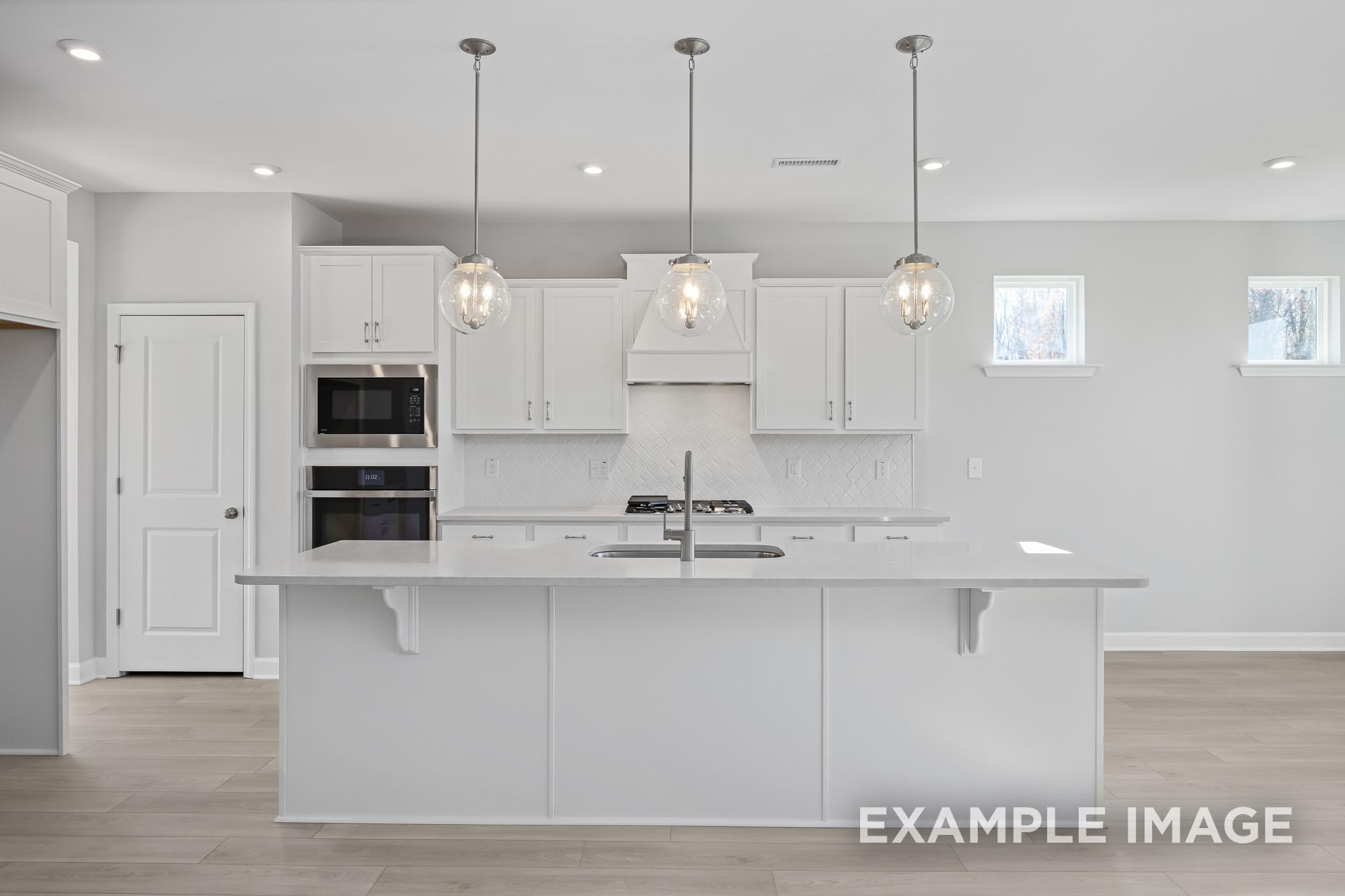 Spacious modern kitchen in The Cypress C II with white shaker cabinets, large island sink, stainless steel appliances, and pendant lights