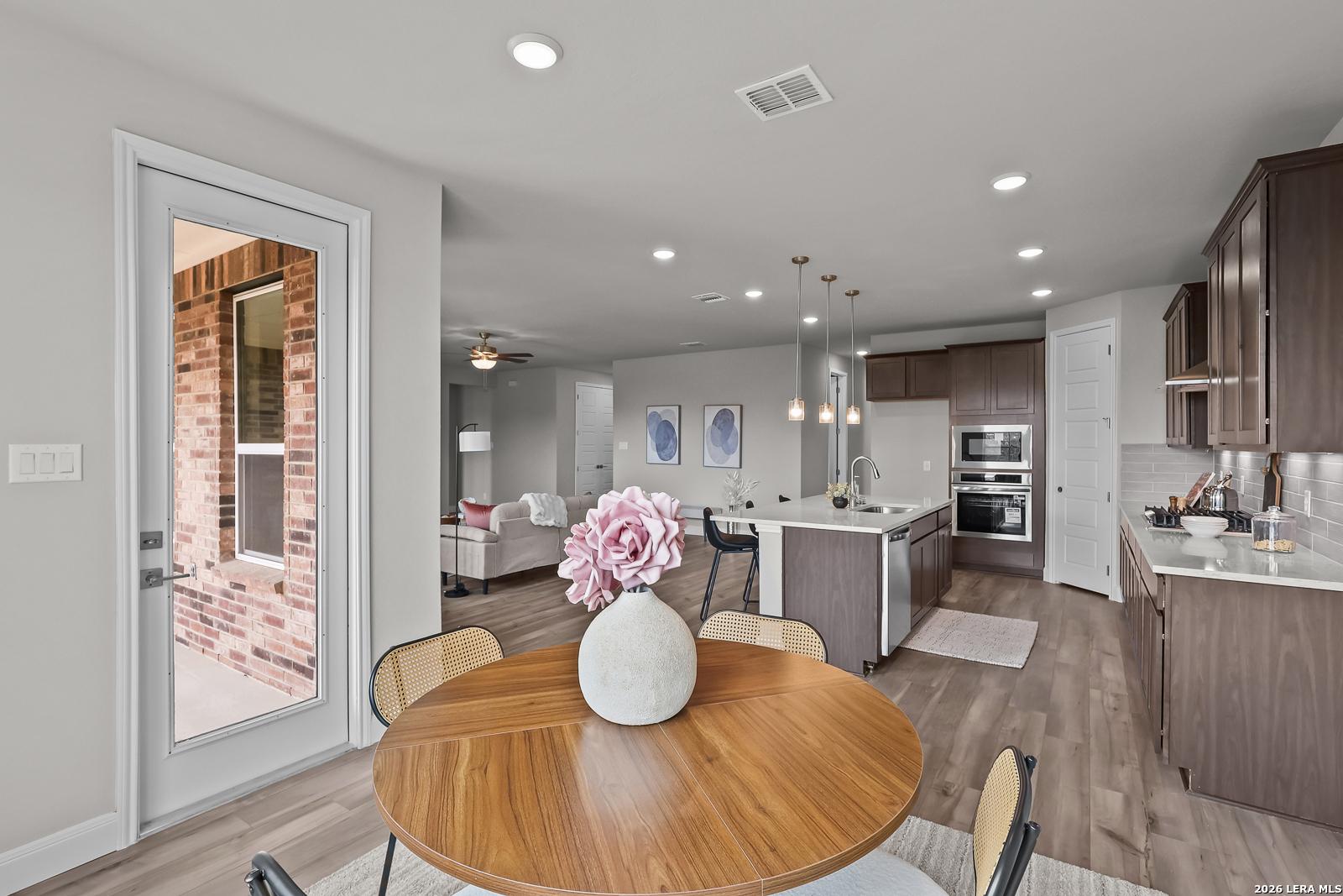 Bright open-concept kitchen with white cabinets, quartz island, stainless appliances, and dining table overlooking patio in Davidson Homes The Rockford G, Ladera, San Antonio