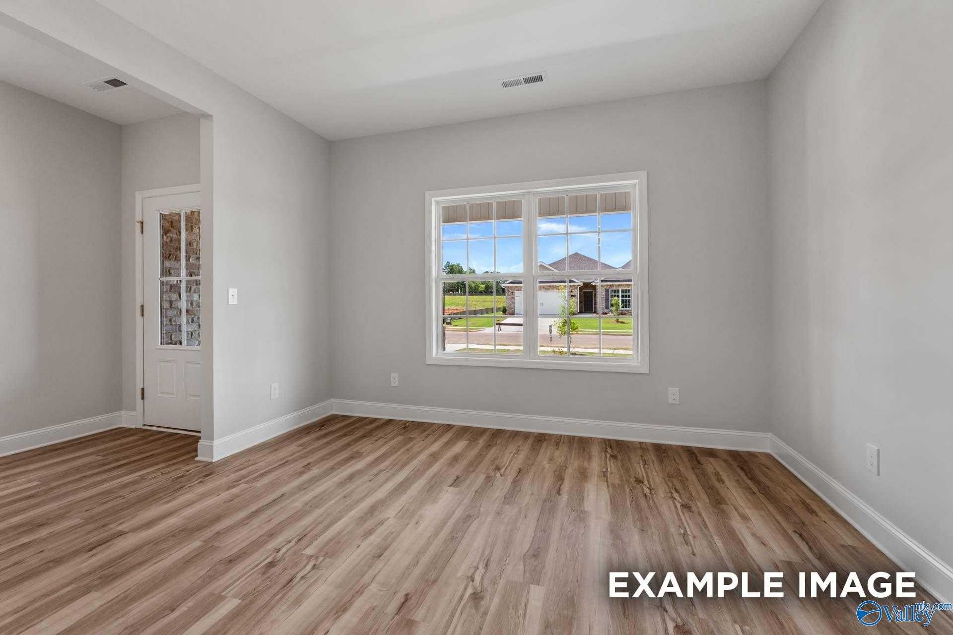 Bright empty bedroom with light gray walls, hardwood floors, and large window view of green yard in Davidson Homes The Shelby C, Meridianville, Alabama