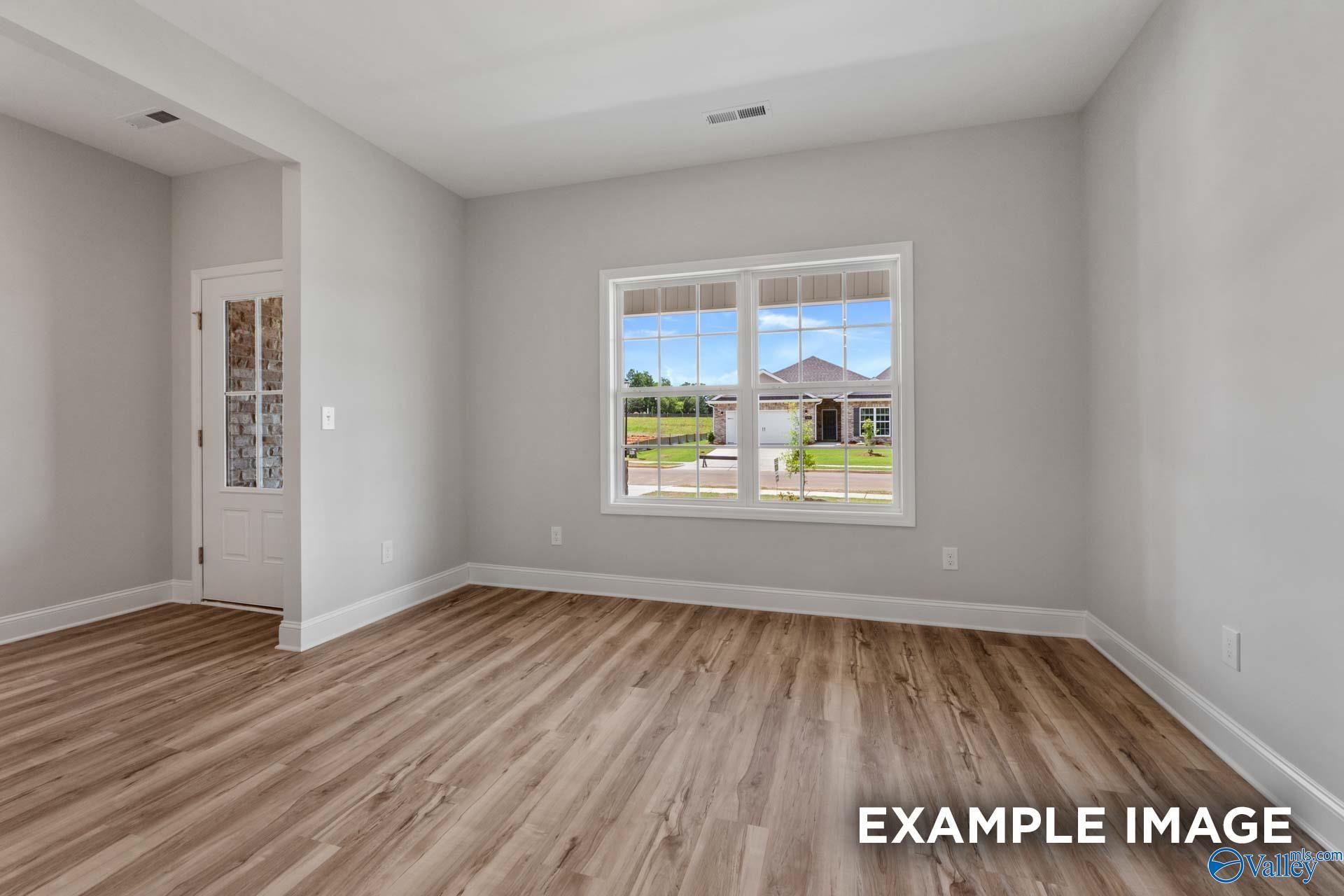 Bright empty bedroom with light gray walls, hardwood floors, and large window view of green yard in Davidson Homes The Shelby C, Meridianville, Alabama