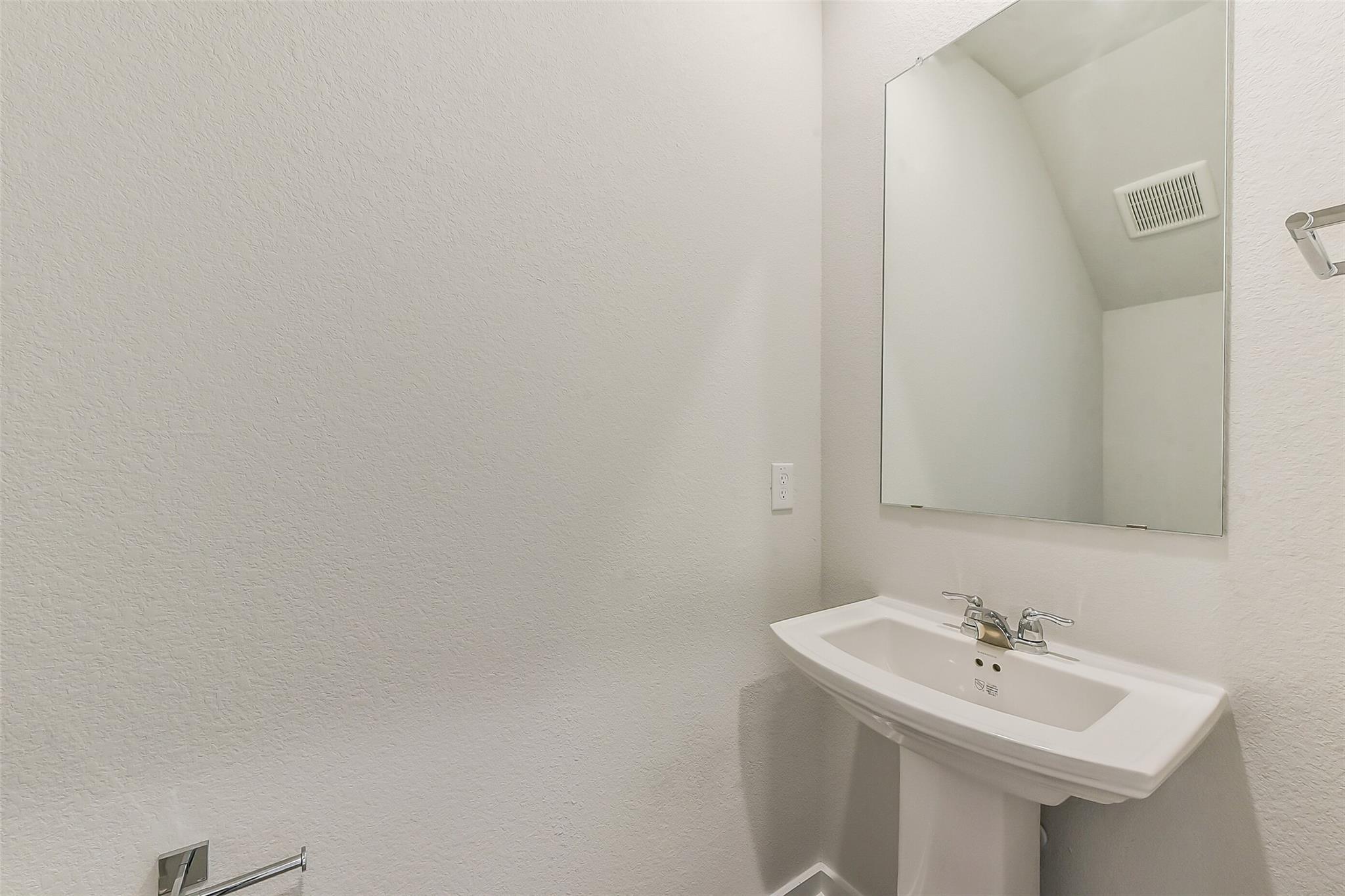 White pedestal sink and frameless mirror in spacious powder room, The Brazos E by Davidson Homes, Windmill Estates, Magnolia TX