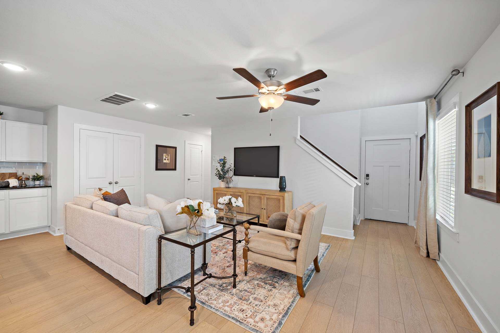 Spacious open-concept living room at Haven at Kieth Harrow in Cypress TX featuring beige sofa, hardwood floors, ceiling fan, and white cabinets by Davidson Homes