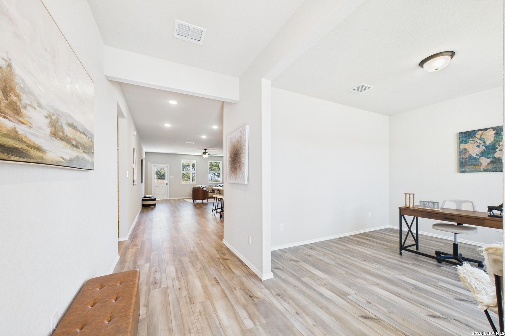 Bright hallway with hardwood floors, abstract wall art, and cushioned bench leading to home office in Davidson Homes Douglas E, Bricewood San Antonio