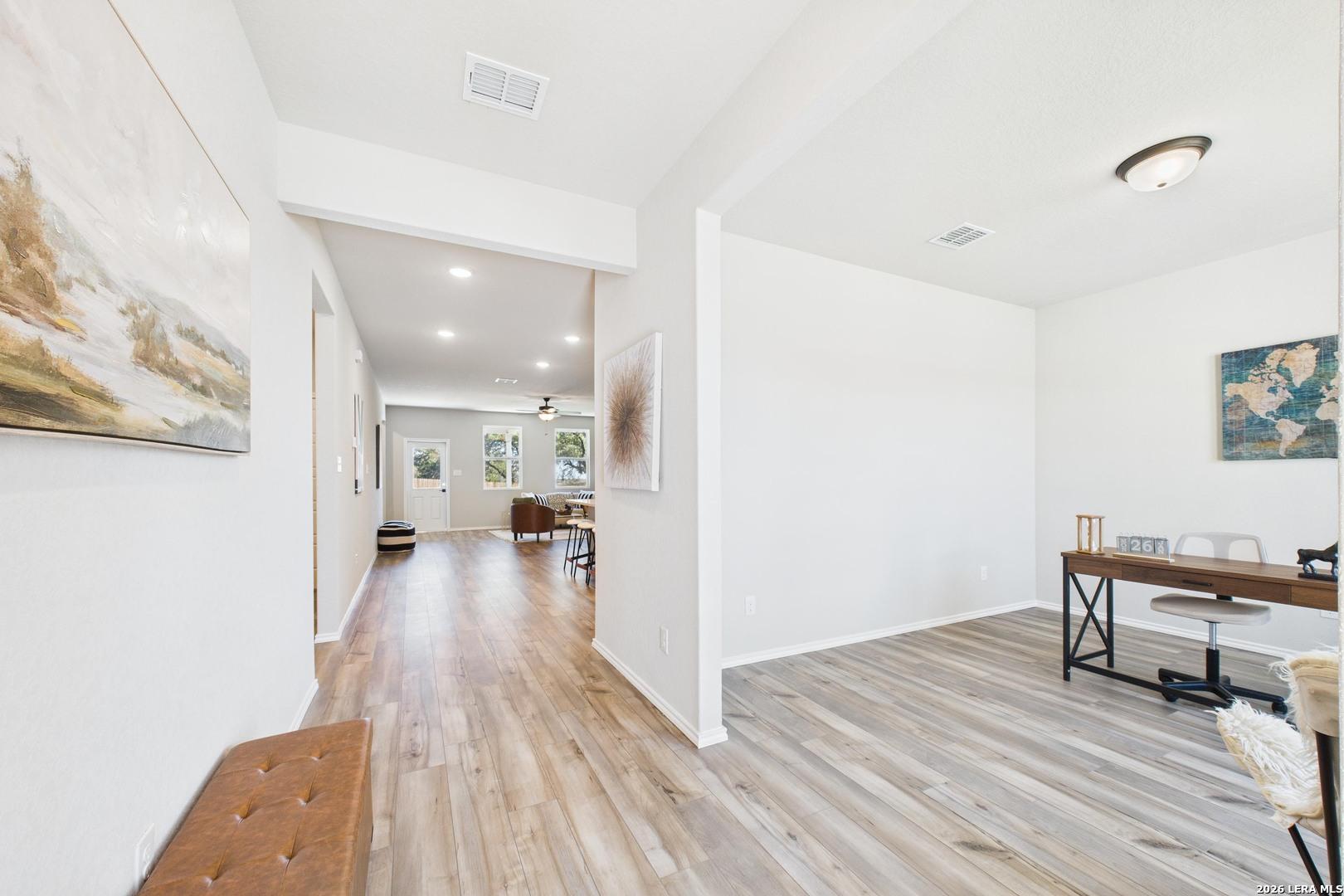 Bright hallway with hardwood floors, abstract wall art, and cushioned bench leading to home office in Davidson Homes Douglas E, Bricewood San Antonio