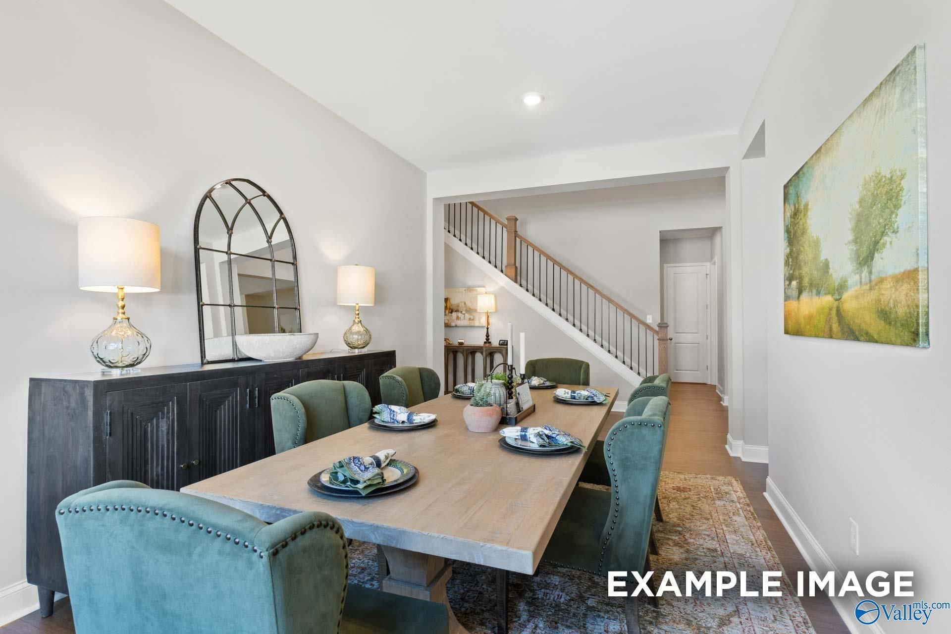 Elegant dining room with farmhouse table, green velvet chairs, arched mirror, and staircase in The Haven E by Evermore Homes, Owens Cross Roads, AL