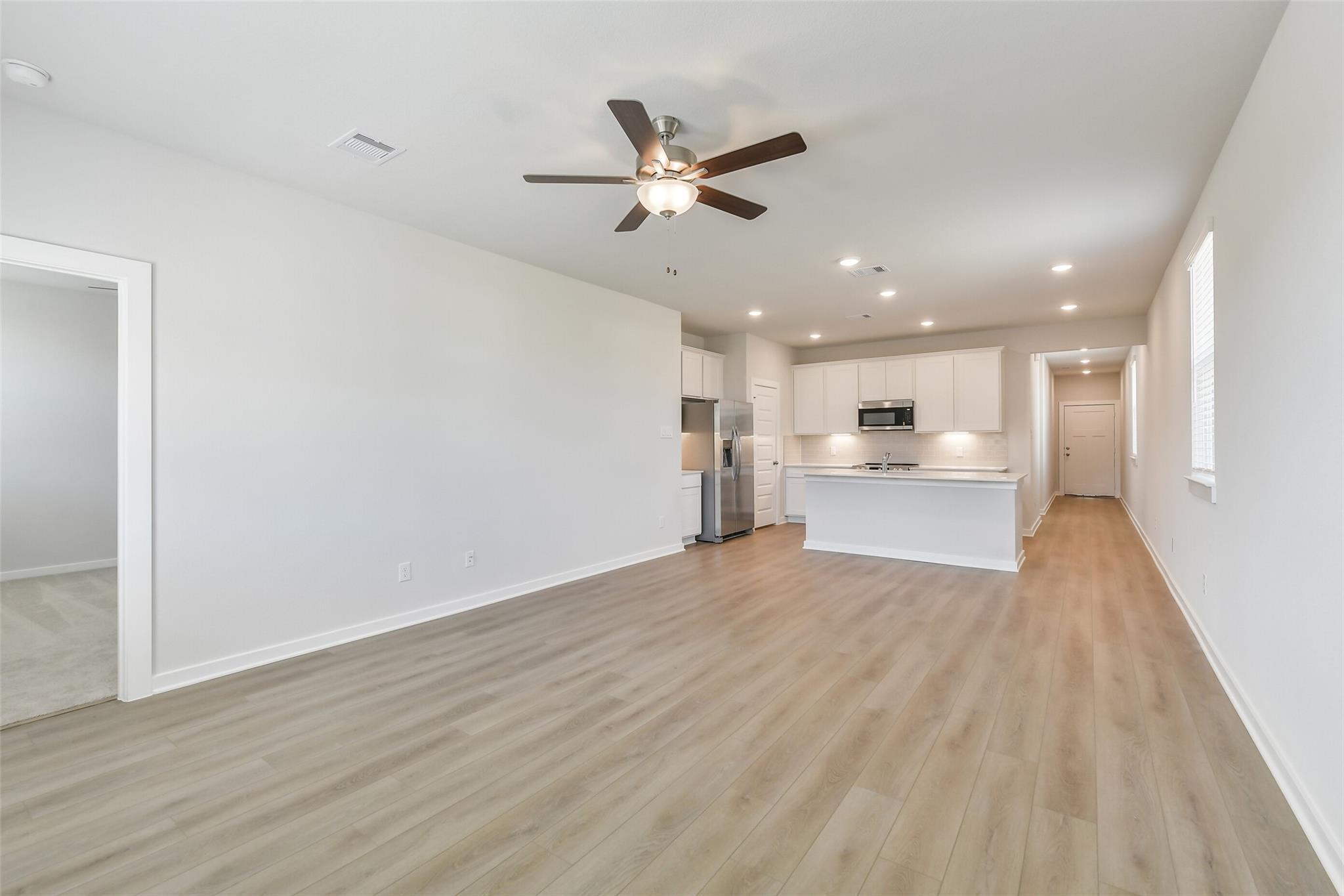 Open-concept kitchen and living area with white cabinets, island, stainless appliances, and ceiling fan in Davidson Homes The Colorado F, Cleveland, Texas